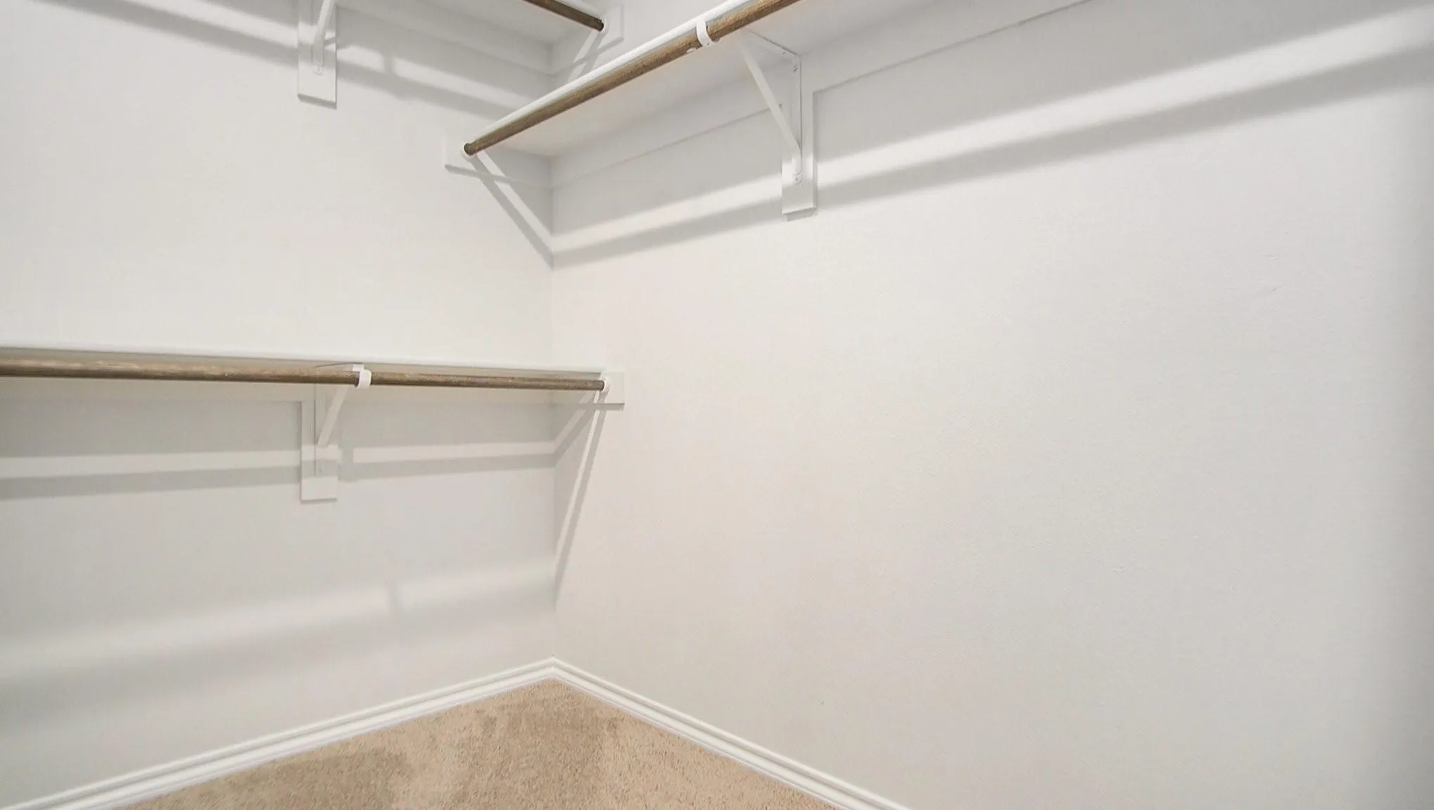 Closet featuring white painted walls, light-colored carpeting, two levels of hanging rods, and integrated shelving