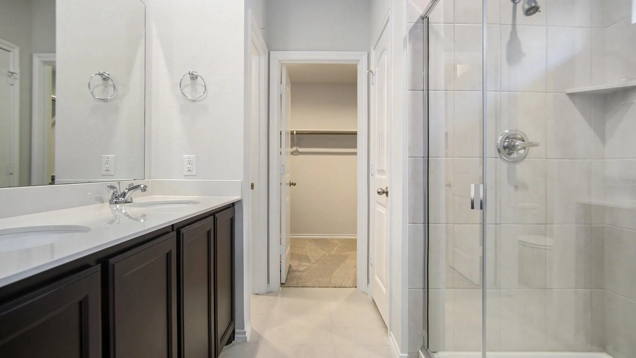 Bathroom featuring a glass-enclosed shower with subway tile surround, a dual vanity with dark wood-finish cabinetry, and white countertops