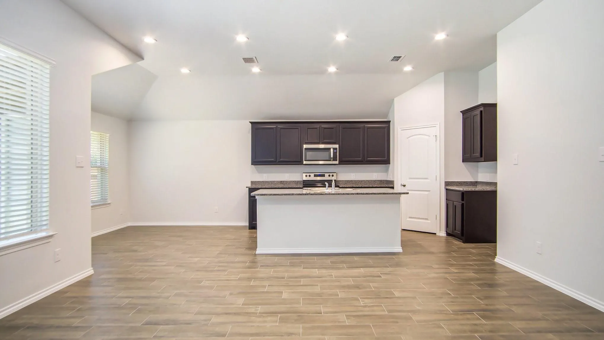 Expansive open-concept living area featuring wood-finish flooring, vaulted ceilings, and recessed lighting