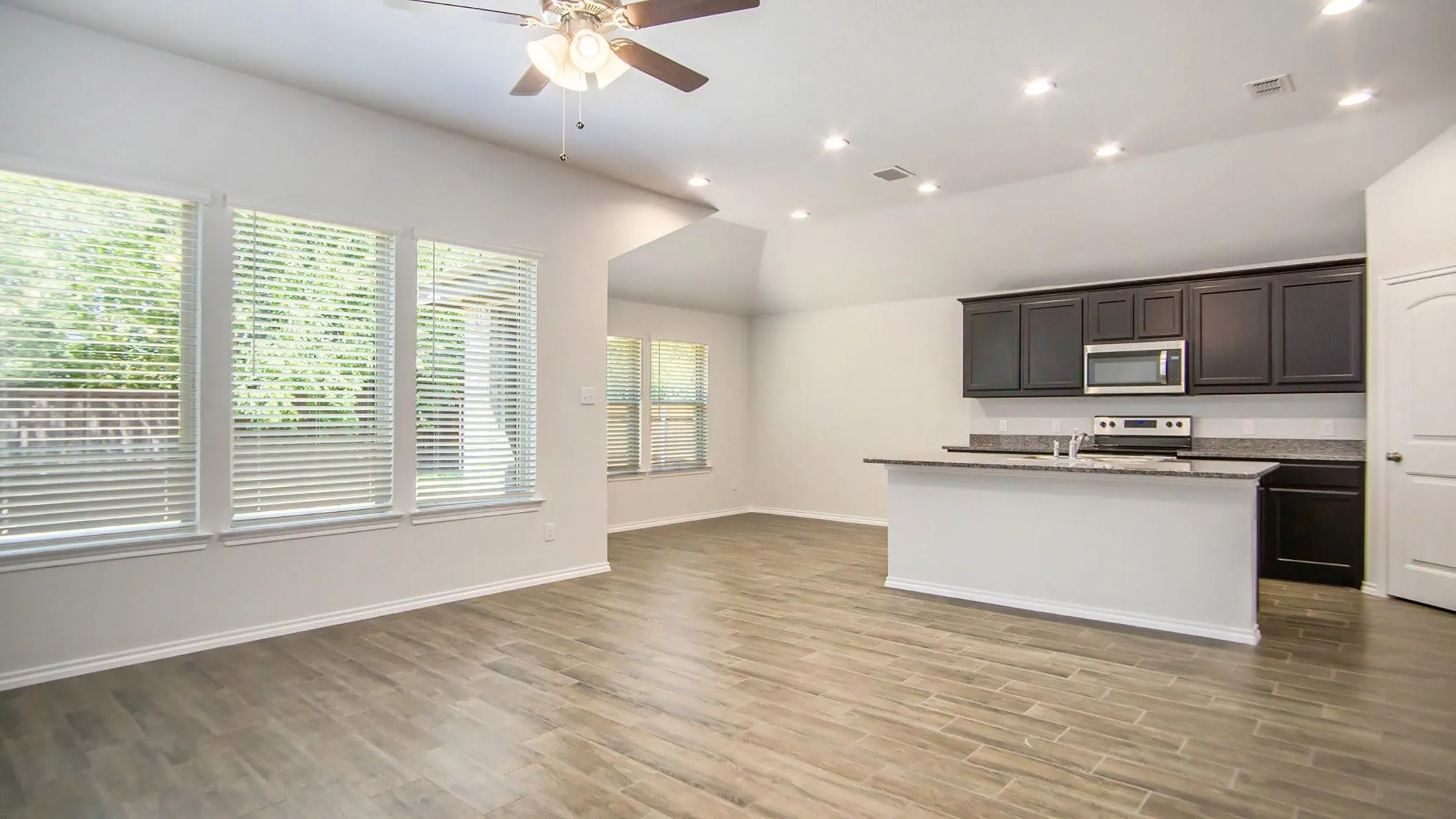 Open-concept living area featuring wood-finish flooring, a contemporary ceiling fan, and a kitchen island with stone countertops