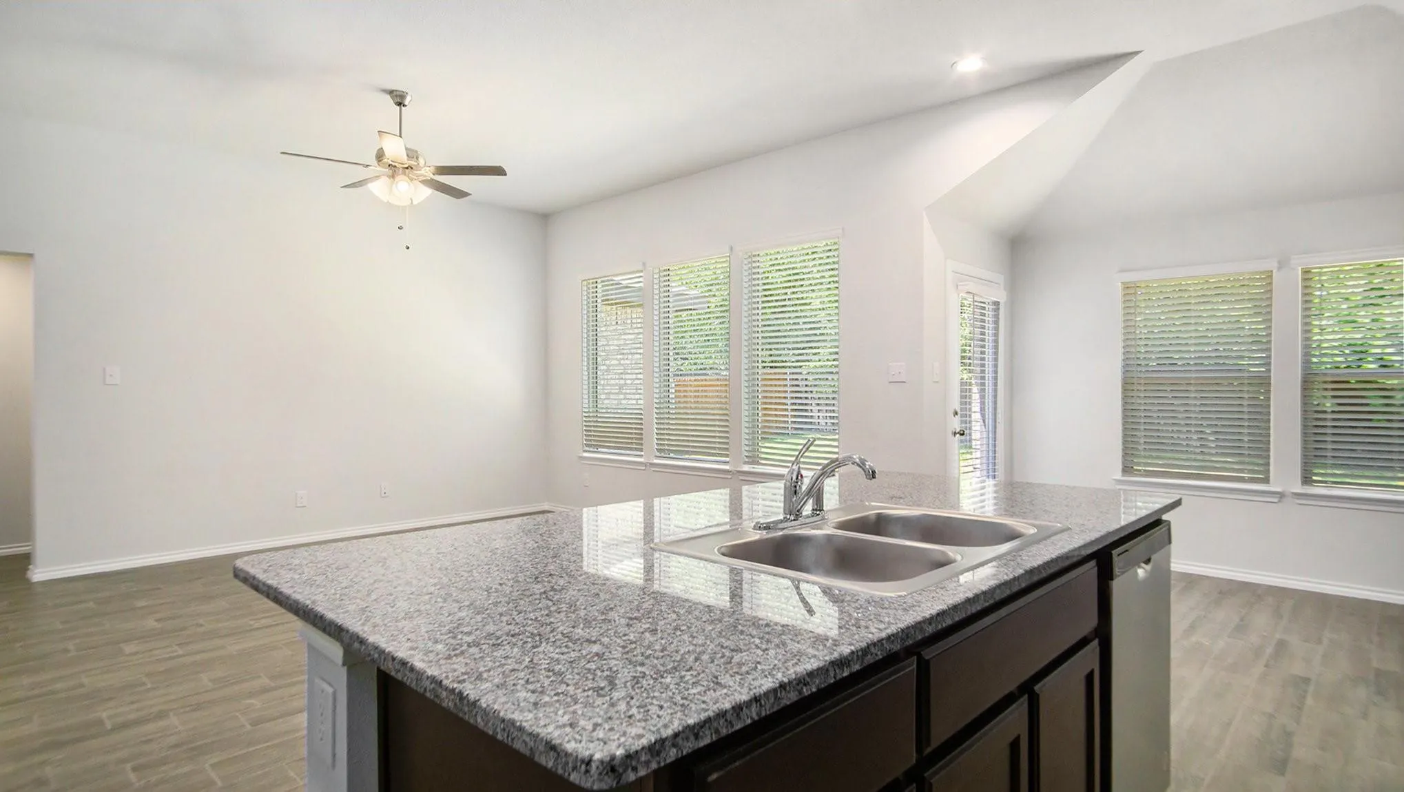 Kitchen island featuring a double basin sink, granite countertop, dark wood-finish cabinetry, and an integrated dishwasher
