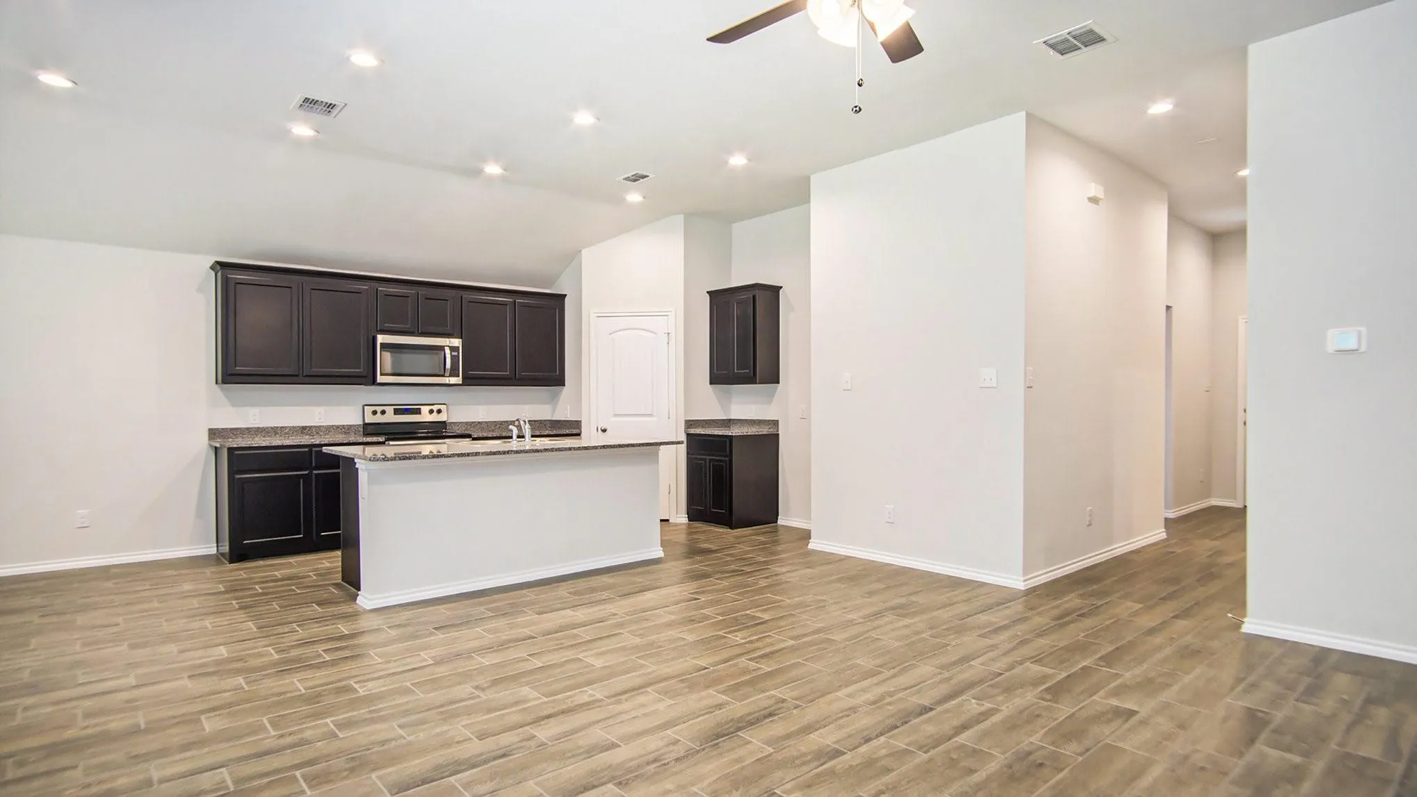 Kitchen and living area featuring wood-finish flooring, dark cabinetry, light countertops, a kitchen island, and recessed lighting