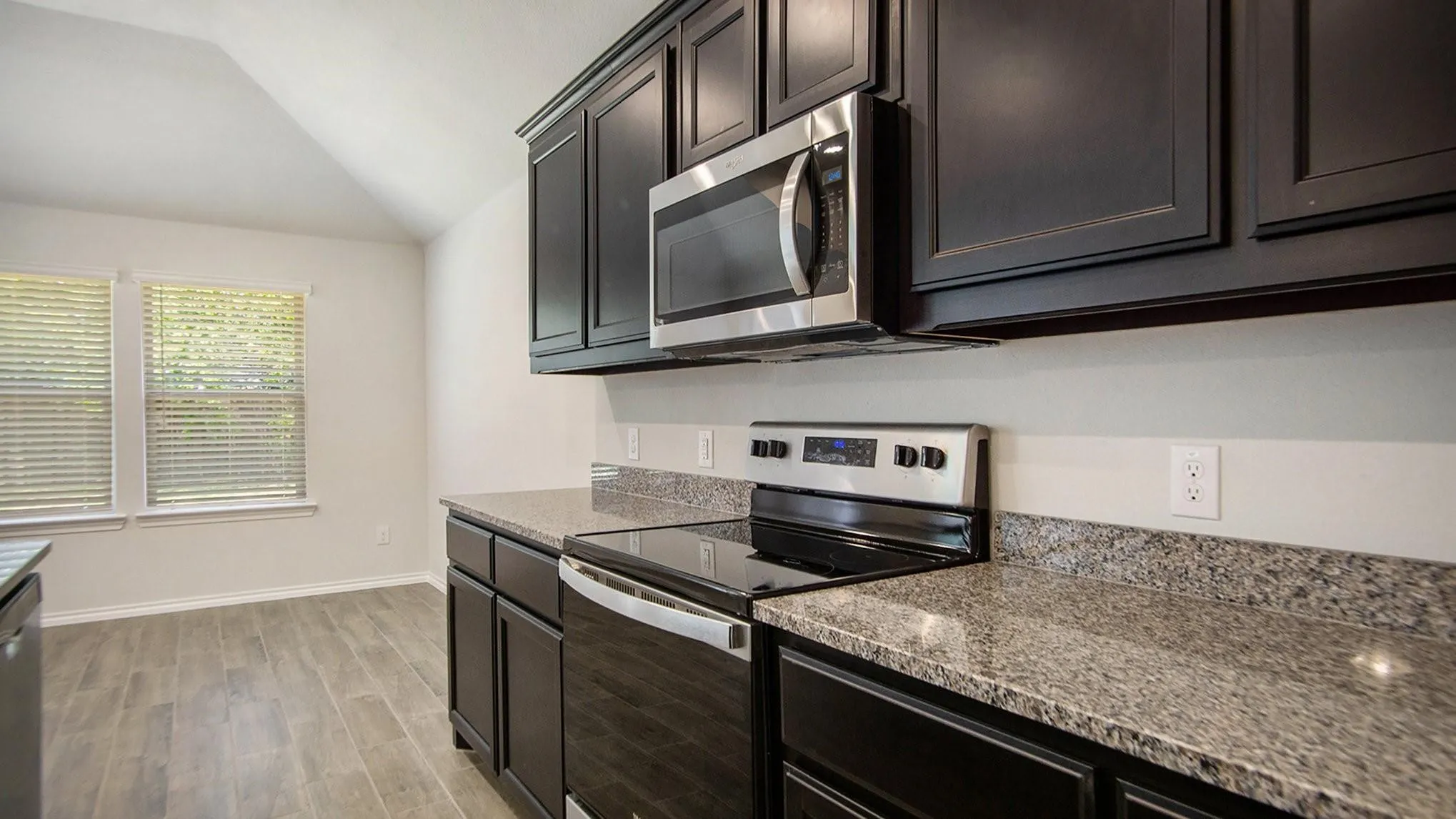 Kitchen featuring dark cabinetry, speckled countertops, stainless steel appliances, and wood-finish flooring