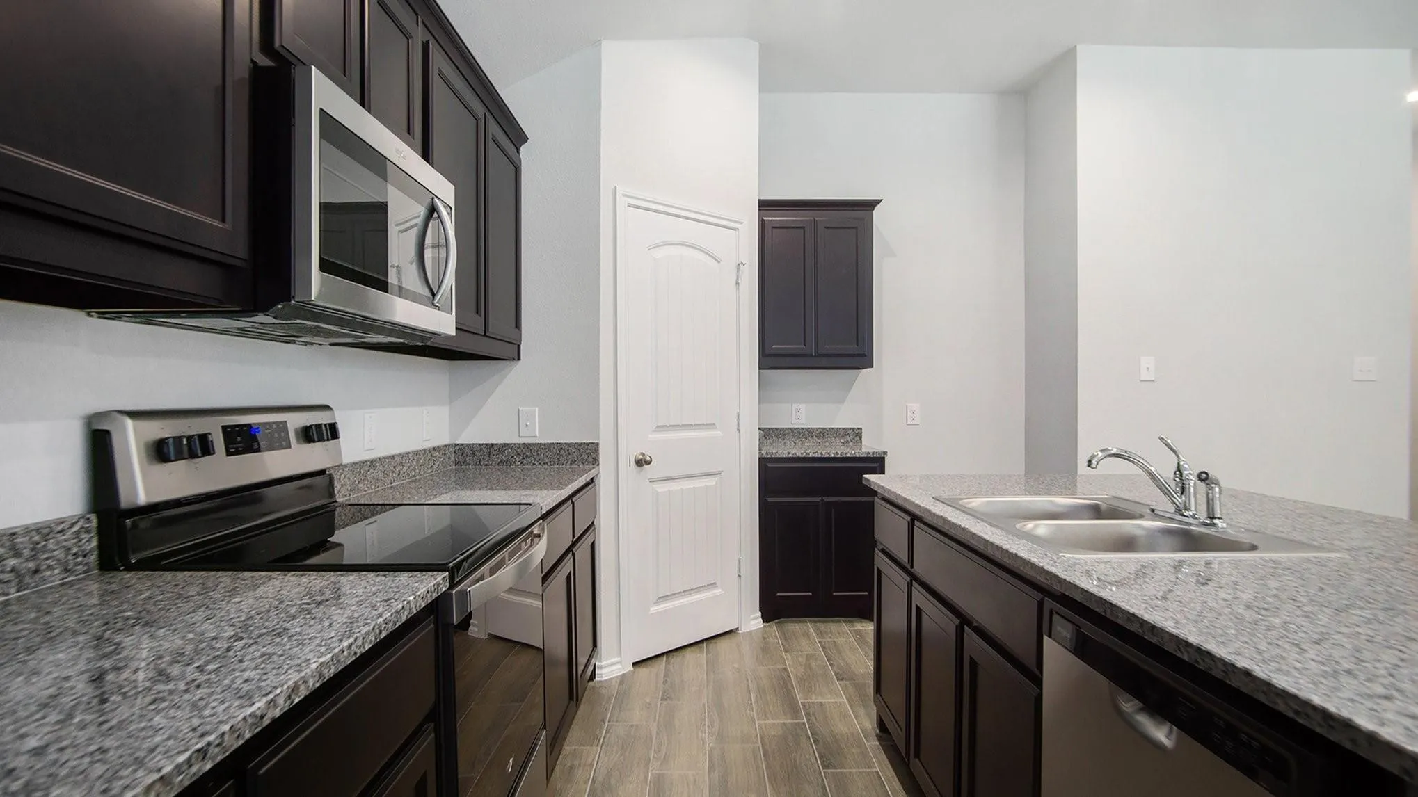 Kitchen featuring dark wood cabinetry, light grey granite countertops, stainless steel appliances, and wood-finish tile flooring