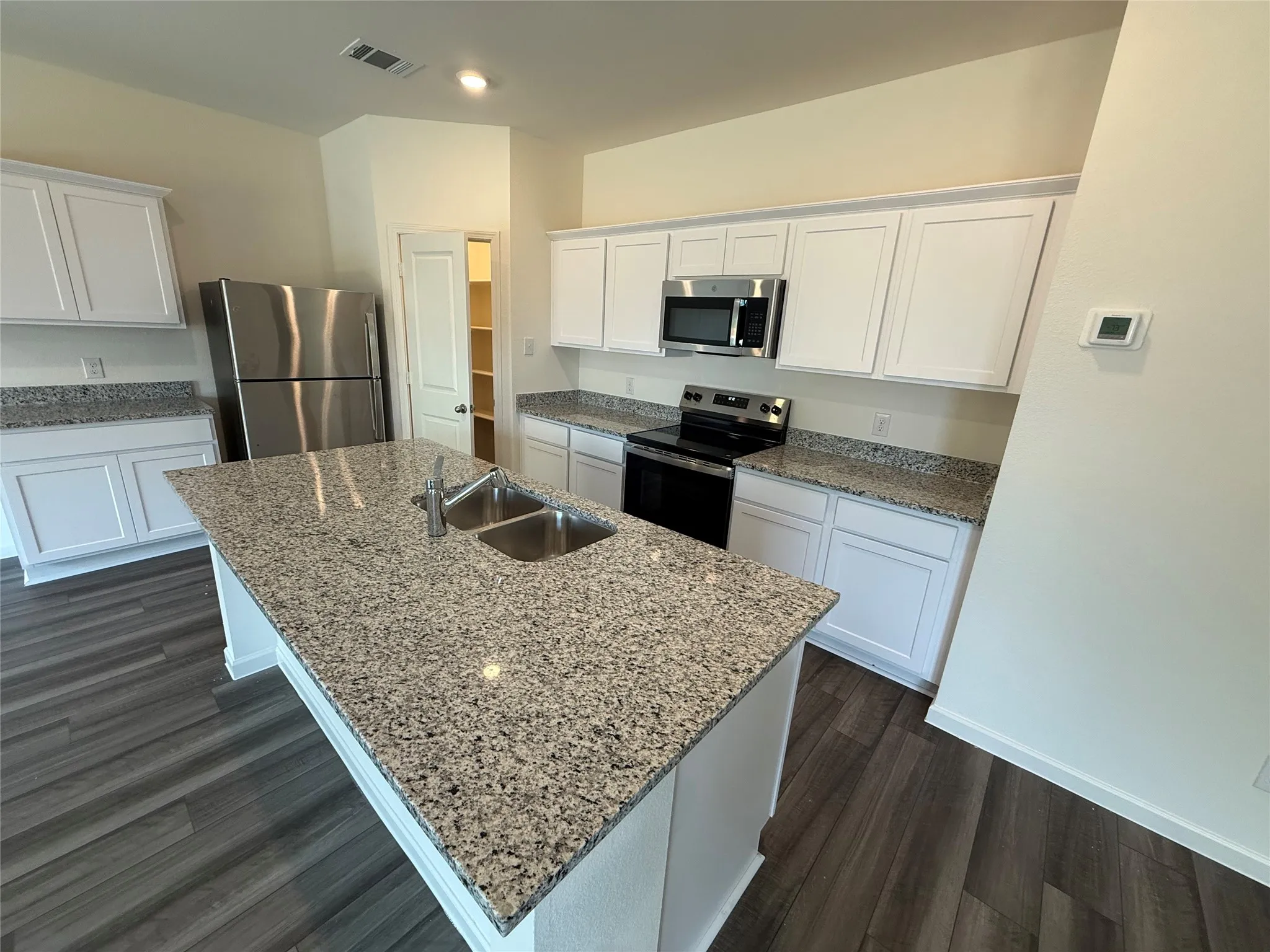 Kitchen featuring a center island with an integrated double basin sink, stainless steel appliances, white cabinetry, and wood-finish flooring