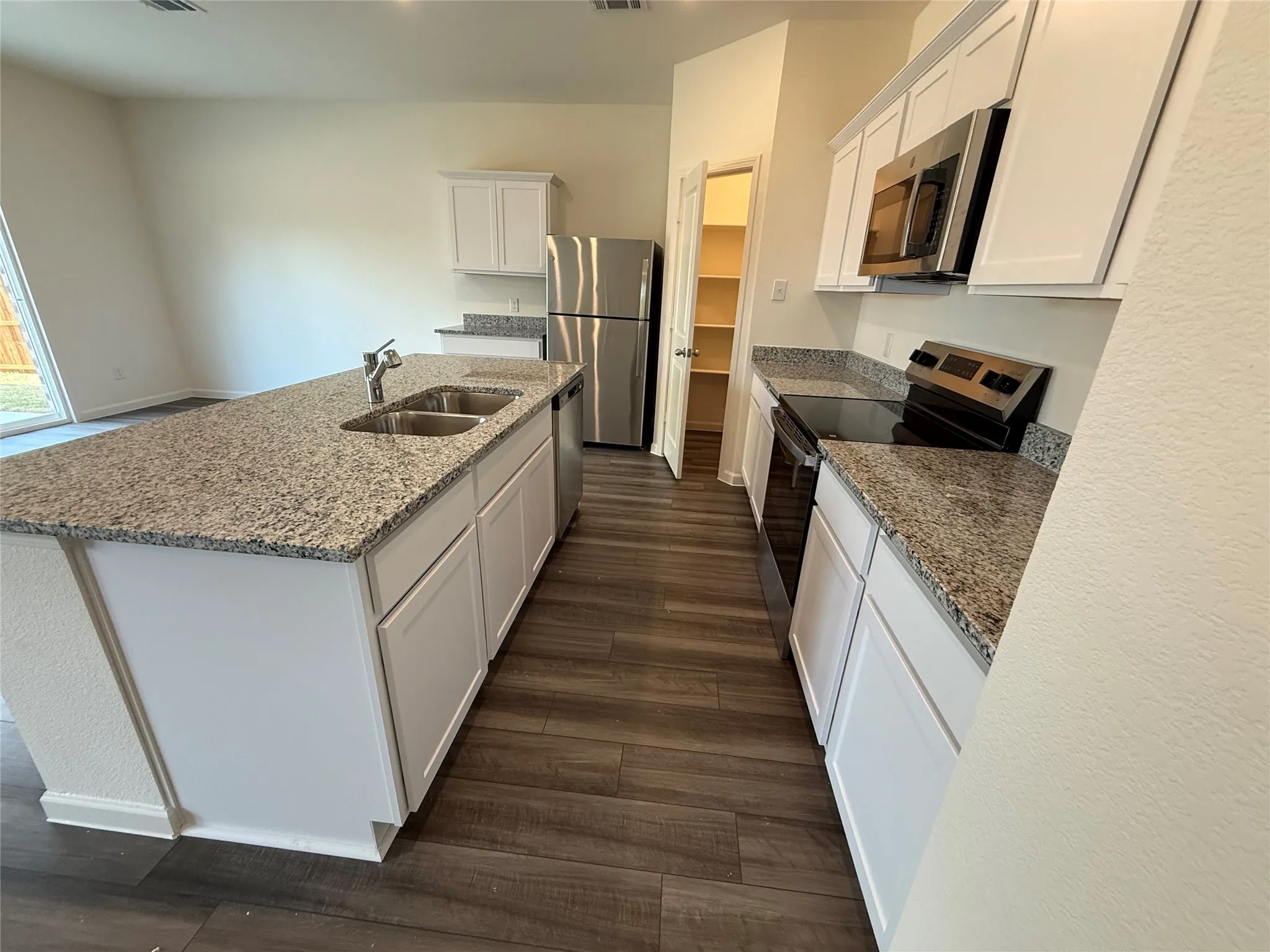 Kitchen featuring white cabinetry, granite countertops, stainless steel appliances, a center island with double sinks, and wood-finish flooring