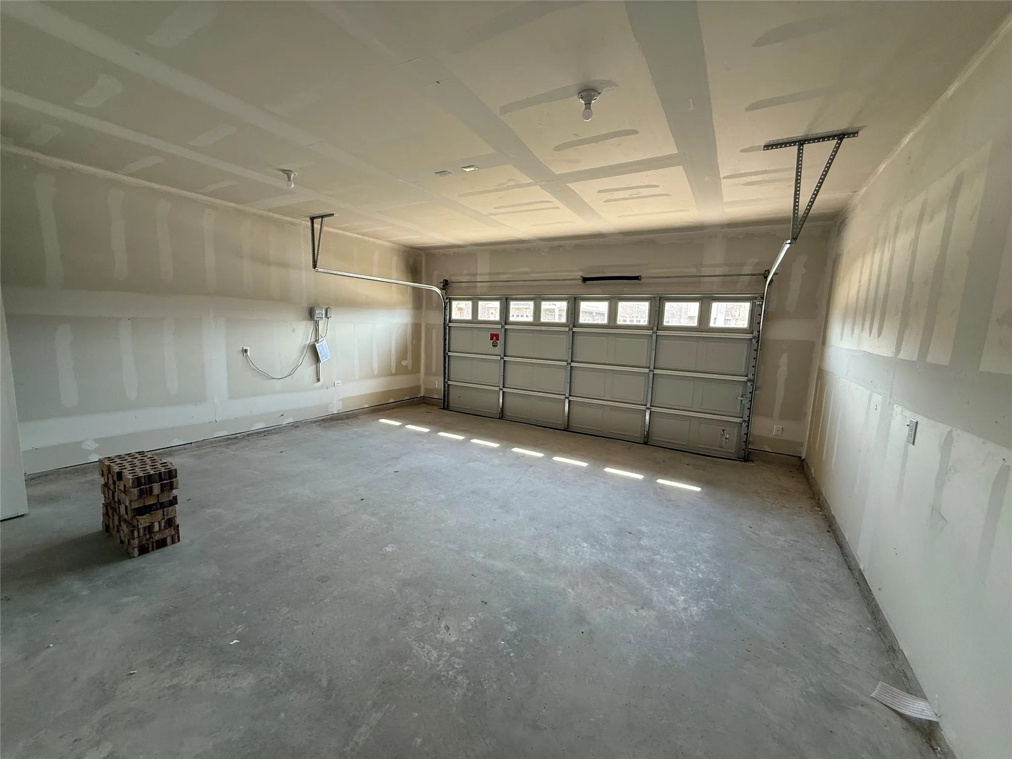 Spacious garage with an overhead door, concrete flooring, and ceiling-mounted lighting fixtures