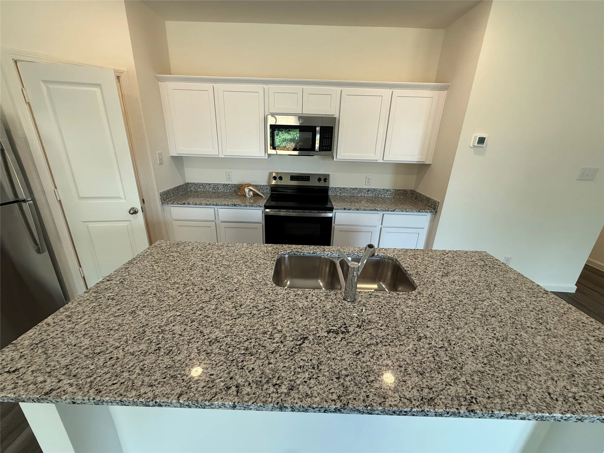 Kitchen featuring a central island with double stainless steel sinks, granite countertops, white cabinetry, and stainless steel appliances including an oven and microwave