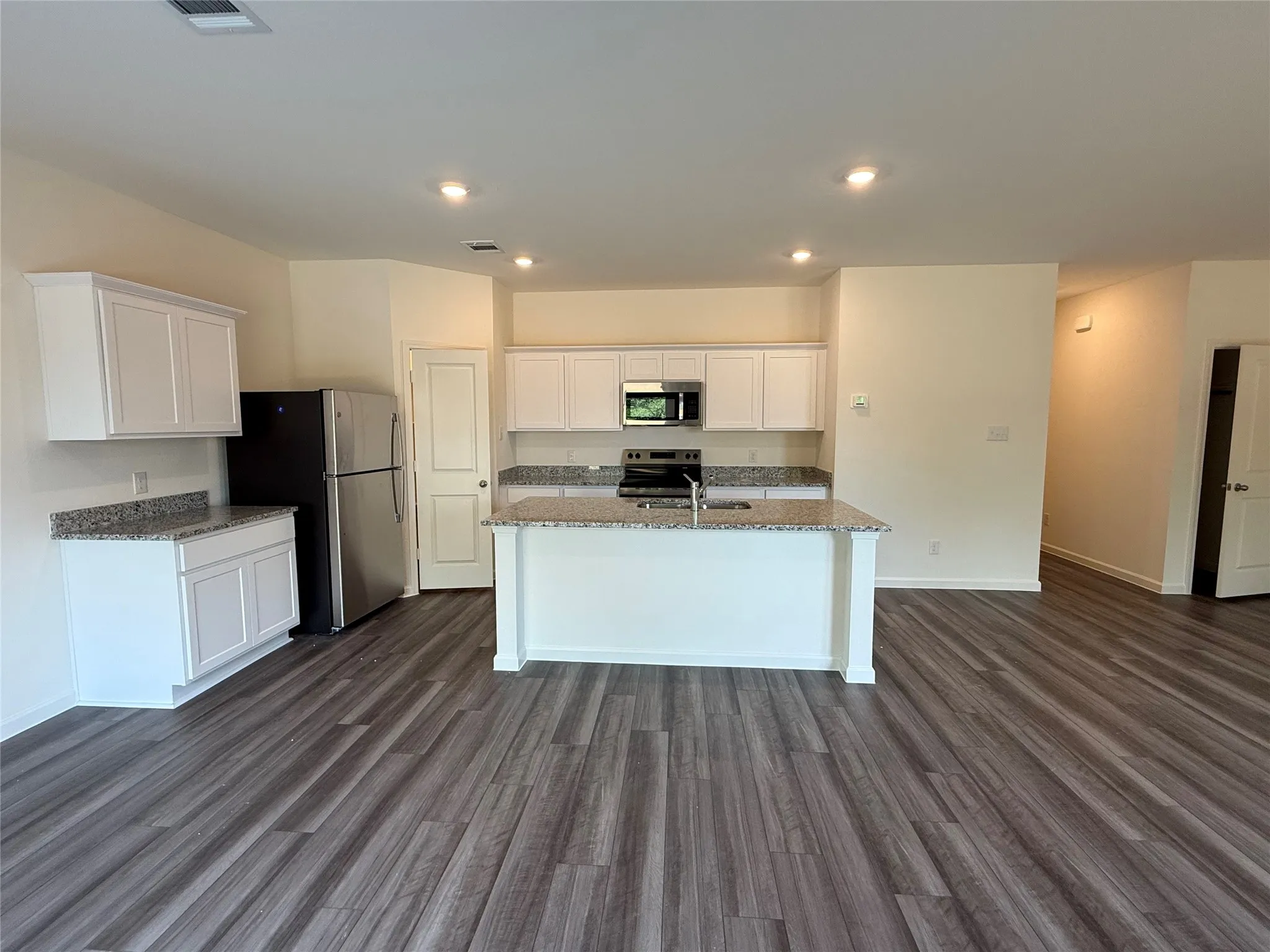 Kitchen with an island featuring a stainless steel sink, white cabinetry, granite-style countertops, and wood-finish flooring