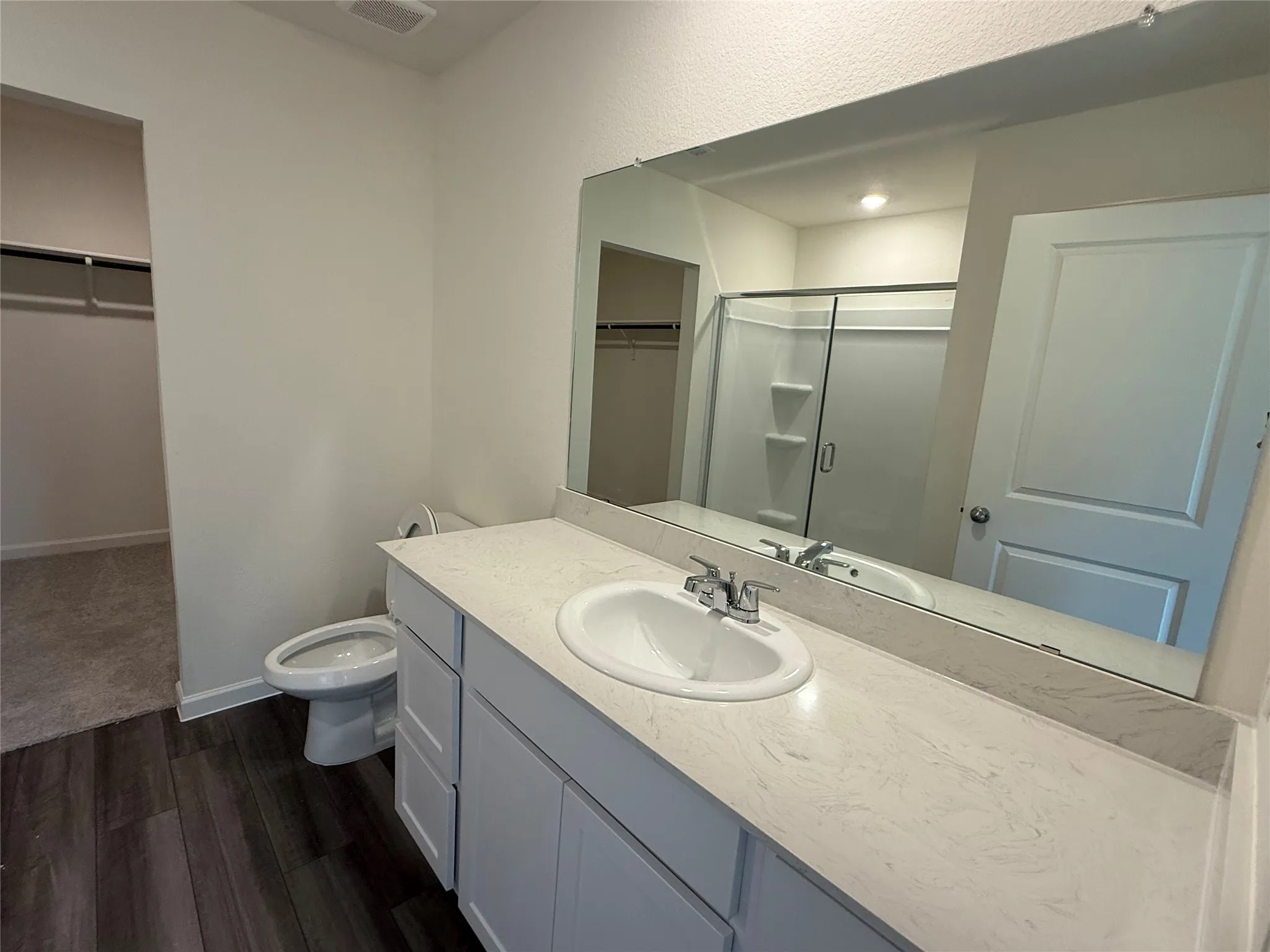 Bathroom featuring a single vanity with a white countertop, wood-finish flooring, and a walk-in shower with a glass enclosure