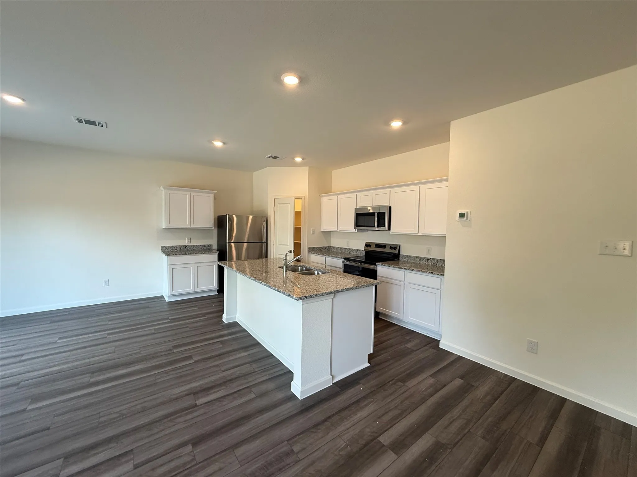 Kitchen featuring a central island, stainless steel appliances, wood-finish flooring, white cabinetry, and recessed lighting