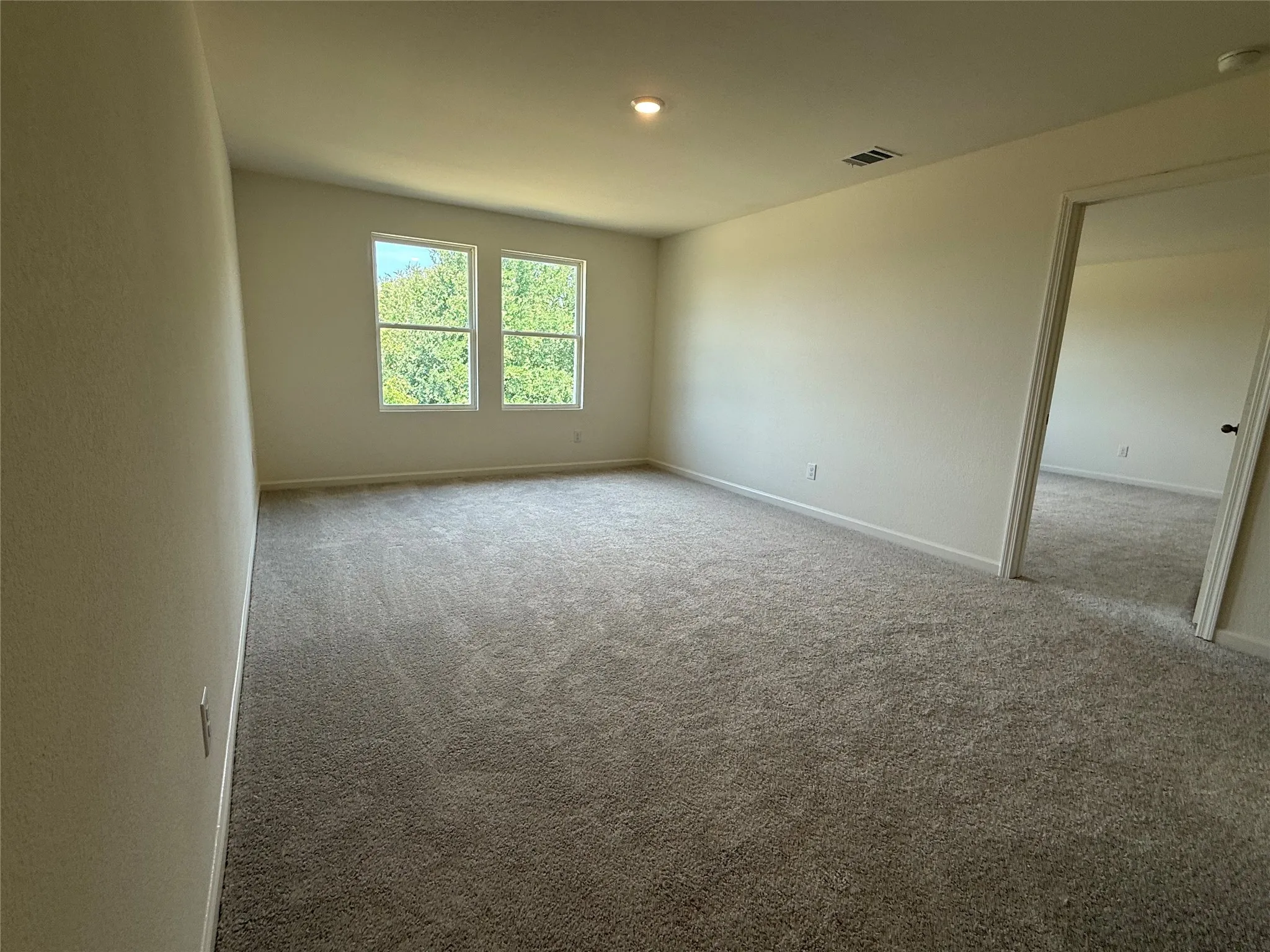 Spacious room featuring neutral carpeting, light-toned wall finishes, two windows providing natural illumination, and a recessed ceiling light fixture