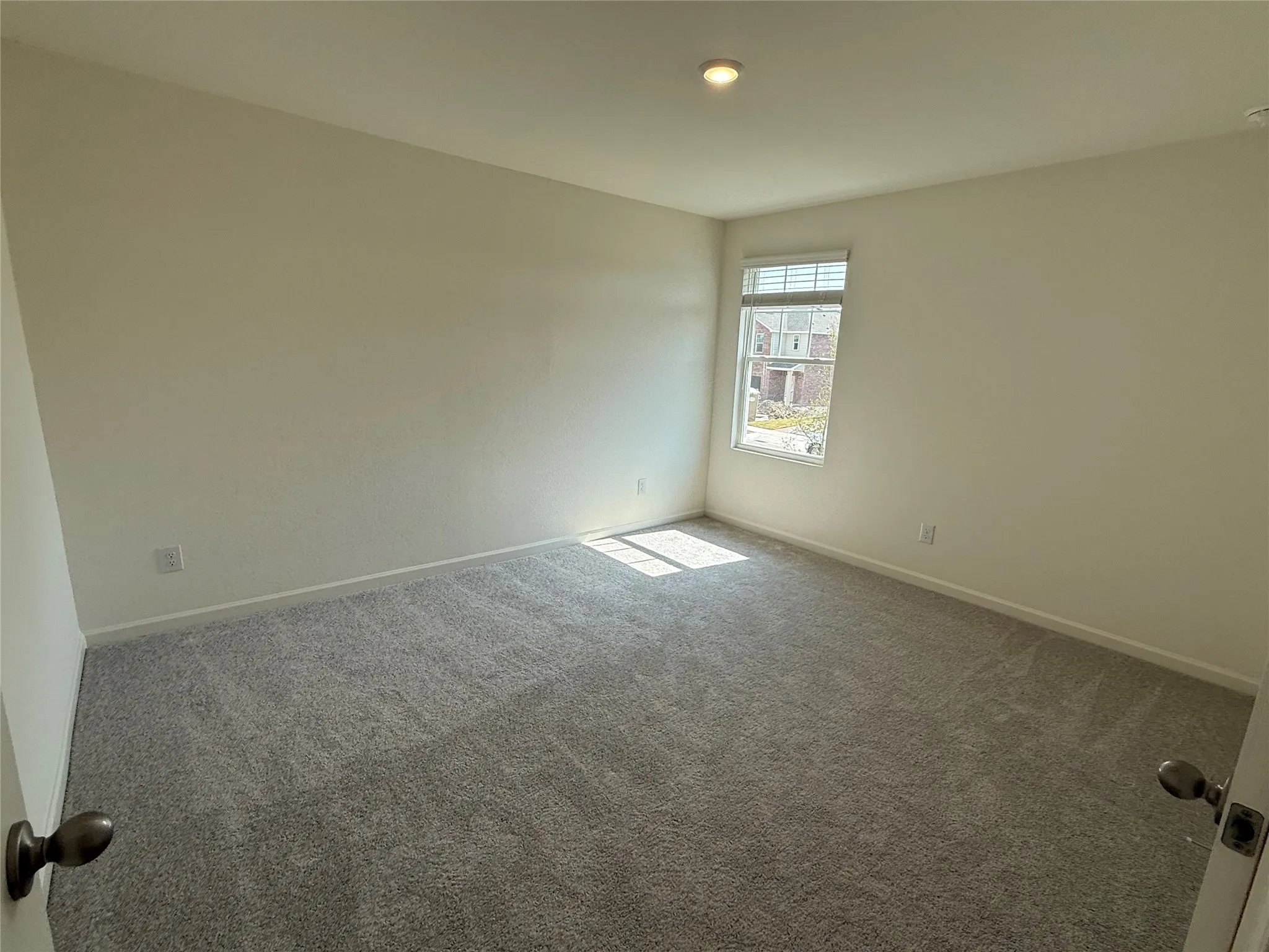 Neutral wall paint with textured finish, recessed lighting, double-hung window with blinds, and gray carpeting