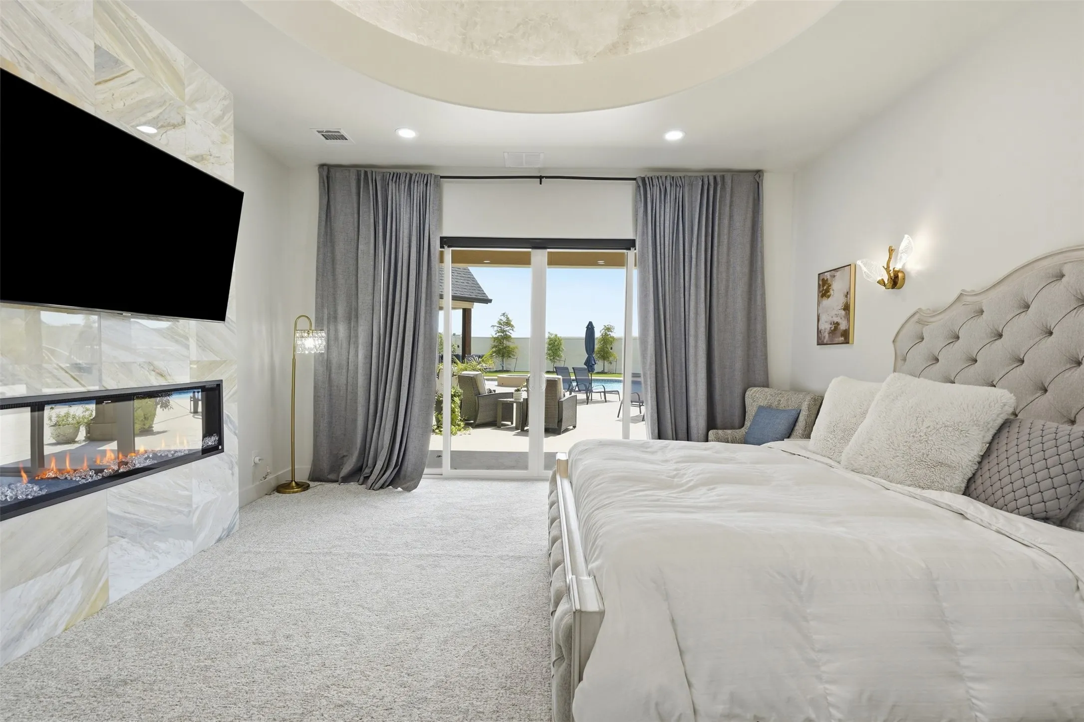 Luxurious primary bedroom featuring a tufted upholstered headboard, recessed ceiling detail, and en-suite access