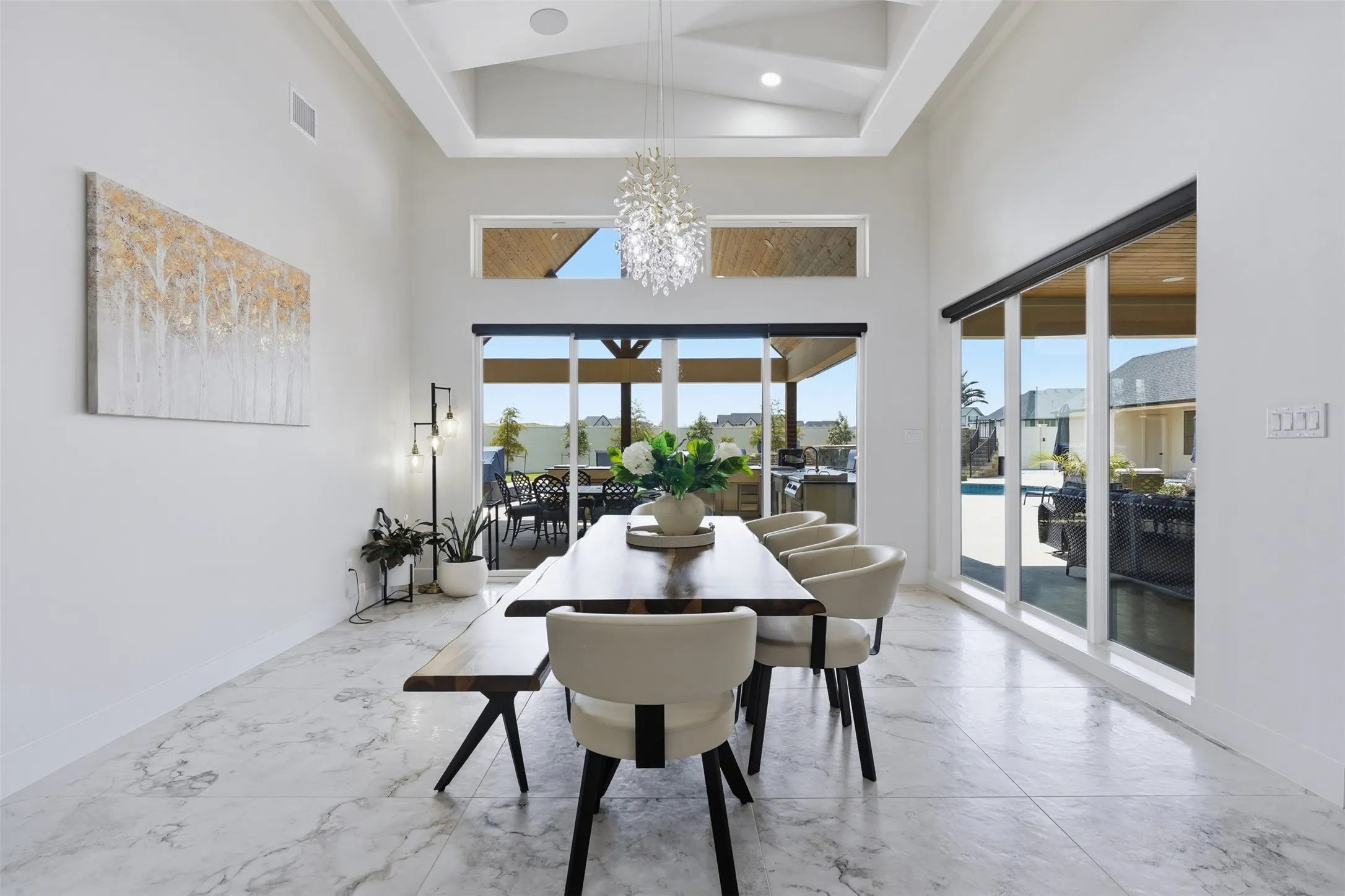 Vaulted ceiling with exposed beams, marble-look tile flooring, large sliding glass doors, and transom windows