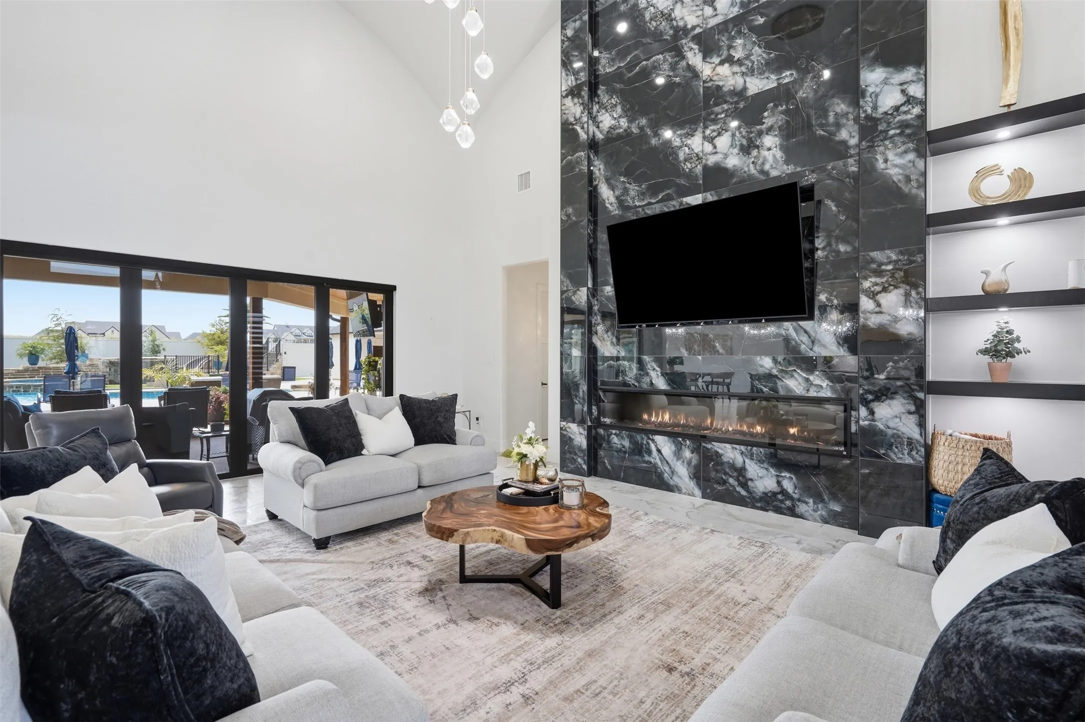 Soaring open-concept living space anchored by a dramatic floor-to-ceiling marble fireplace with integrated linear gas insert and wall-mounted flat-screen television