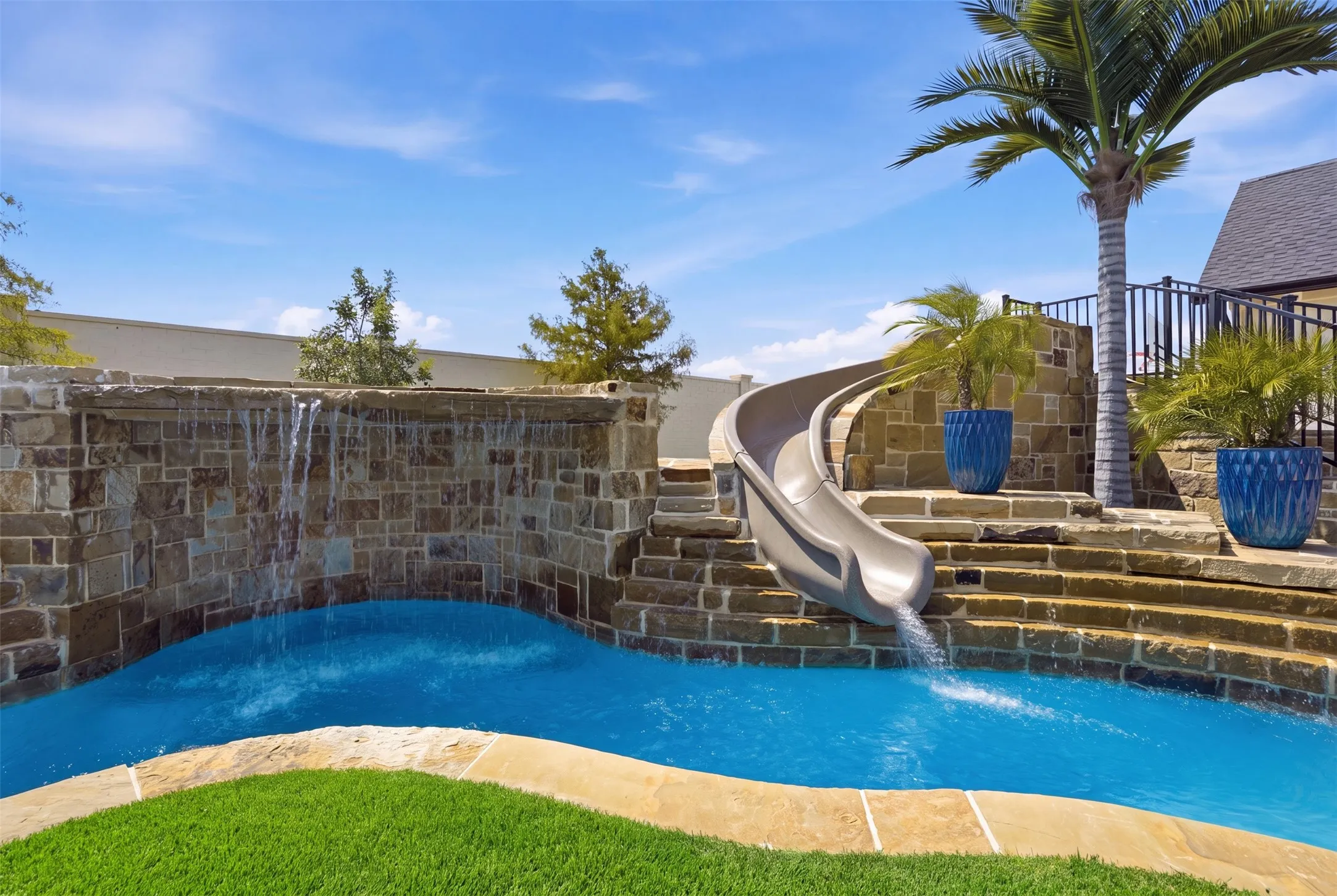 Resort-style pool featuring a built-in water slide, natural stone waterfall, and surrounding stone hardscaping