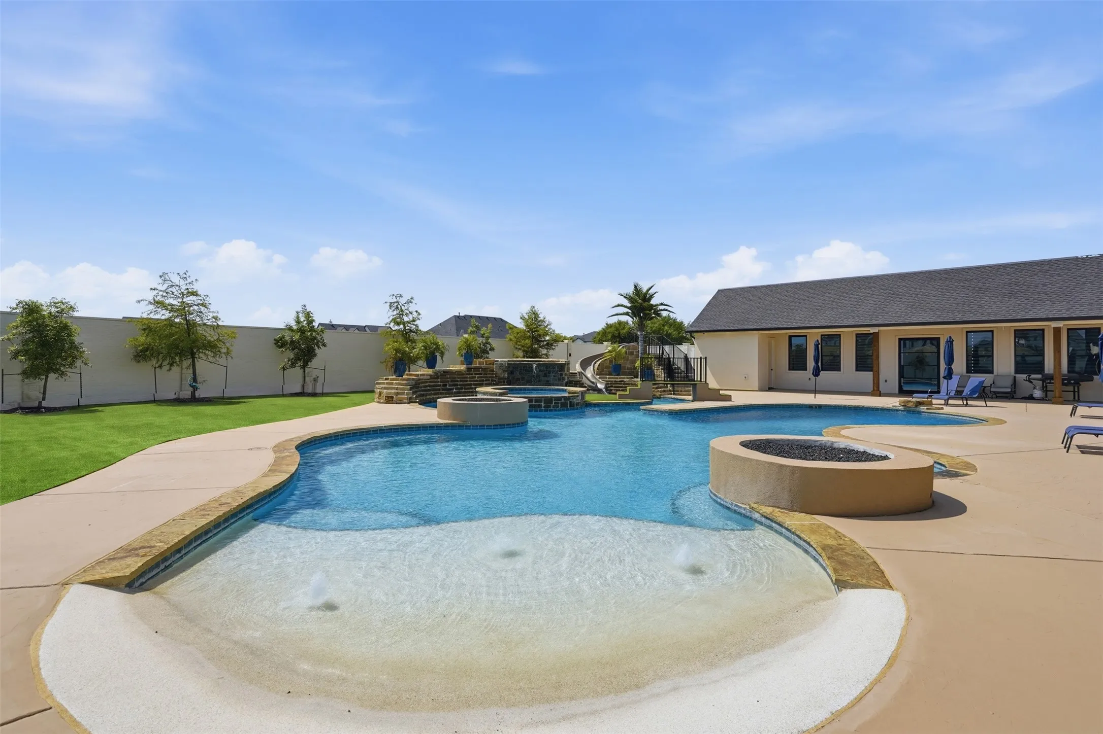 Luxurious resort-style backyard featuring a lagoon-style saltwater pool with shallow sun shelf, circular spa, and integrated water features