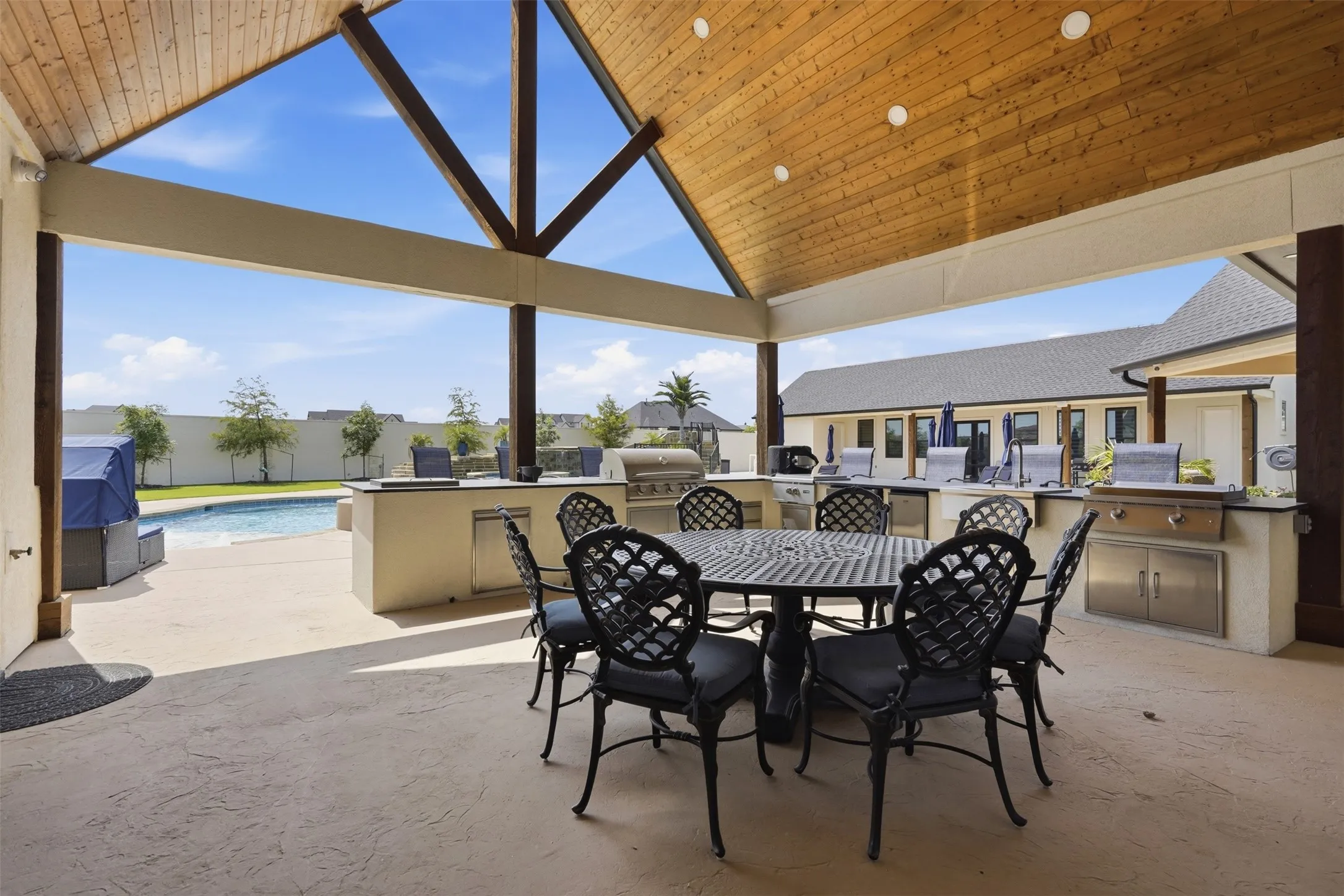 Covered outdoor entertaining space featuring exposed beam ceiling with skylights, built-in grill and countertop cabinetry, and direct pool access