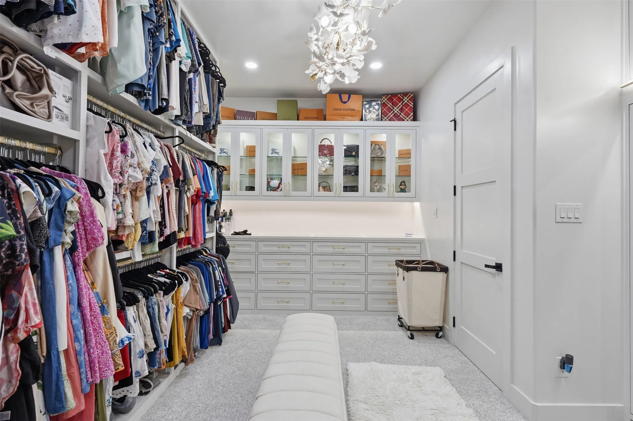 Luxurious walk-in closet featuring extensive built-in cabinetry with multiple drawers and shelving, custom wall-mounted organizers, polished concrete flooring, recessed lighting throughout, and a statement crystal chandelier