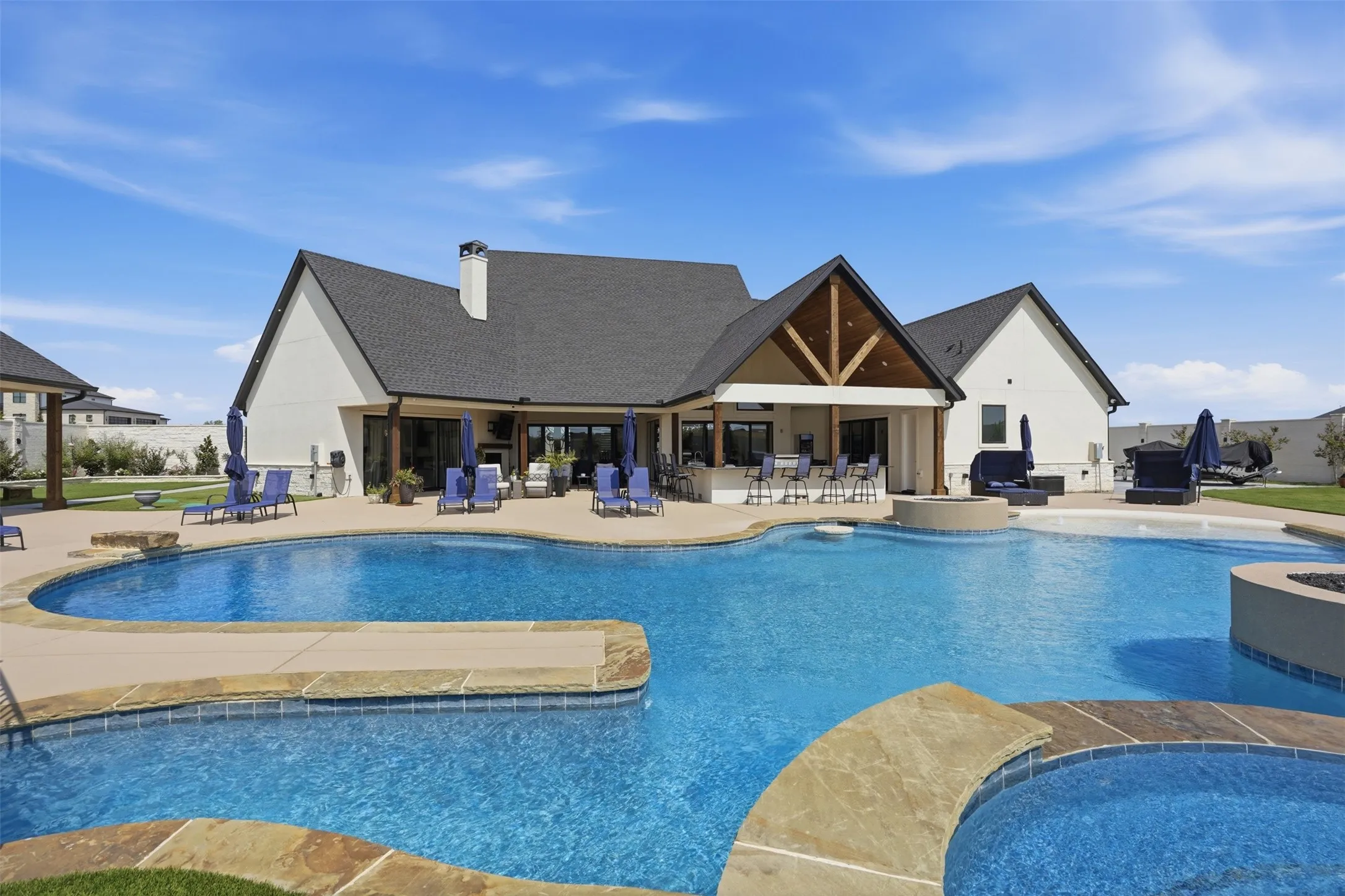 Expansive outdoor living area featuring a large swimming pool, integrated spa, and an outdoor kitchen with bar seating