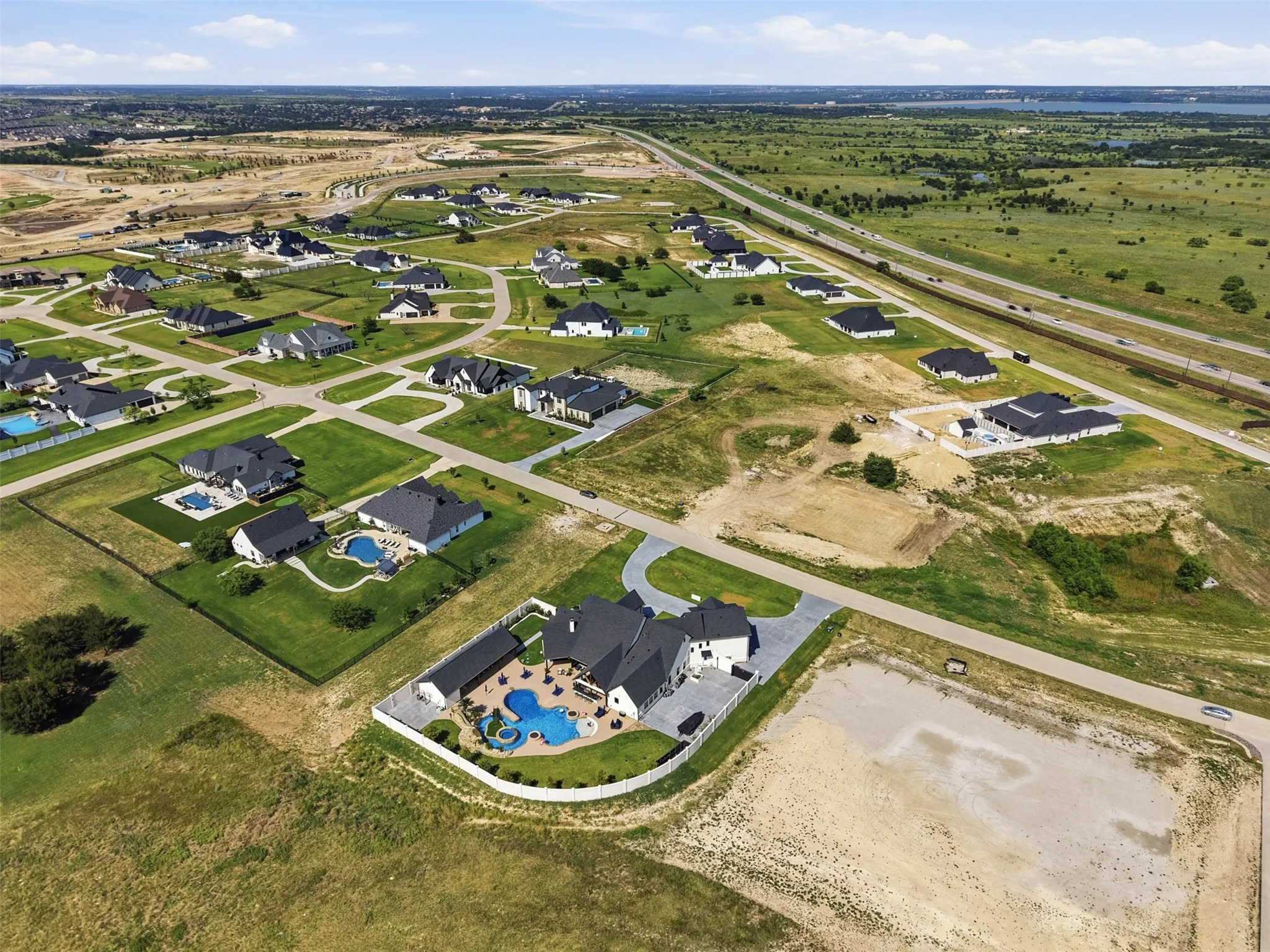 Aerial perspective of a residential neighborhood with landscaped properties, private swimming pools, and paved roadways