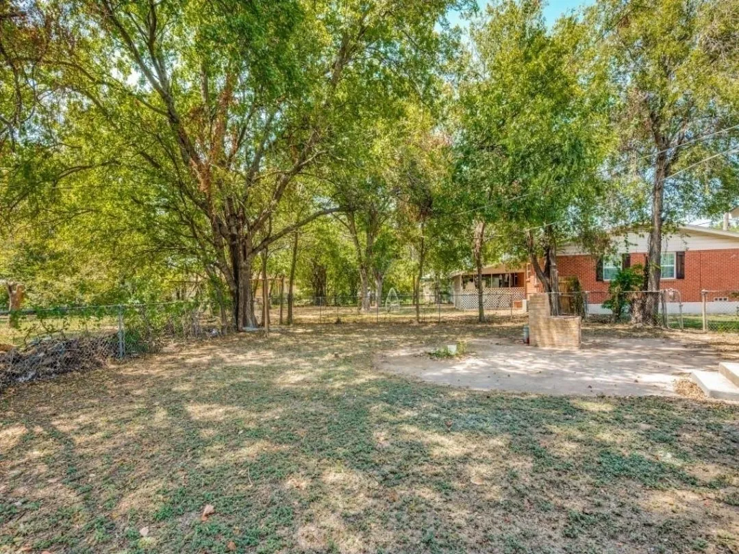 Expansive yard featuring mature trees, a chain-link fence, and a brick-clad outdoor structure