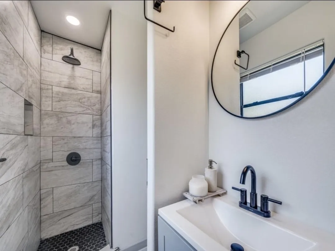 Shower with gray-toned tile walls and black hexagonal floor tiles, featuring a built-in shelf and black rain shower head