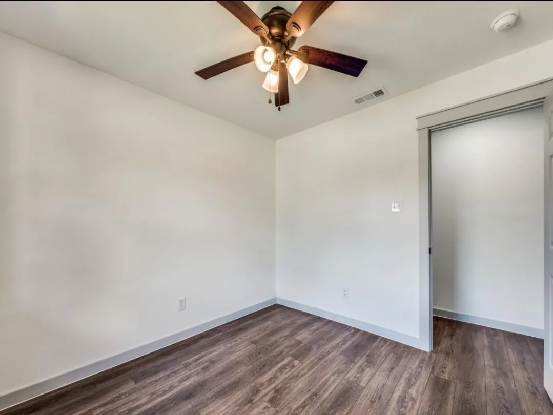 Wood-finish flooring, white walls with gray trim, and a ceiling fan with integrated lighting