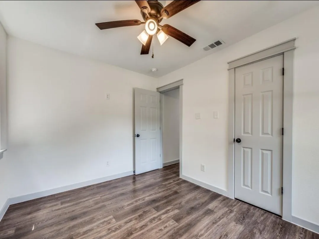 Wood-finish flooring, white walls, and a ceiling fan with integrated lighting