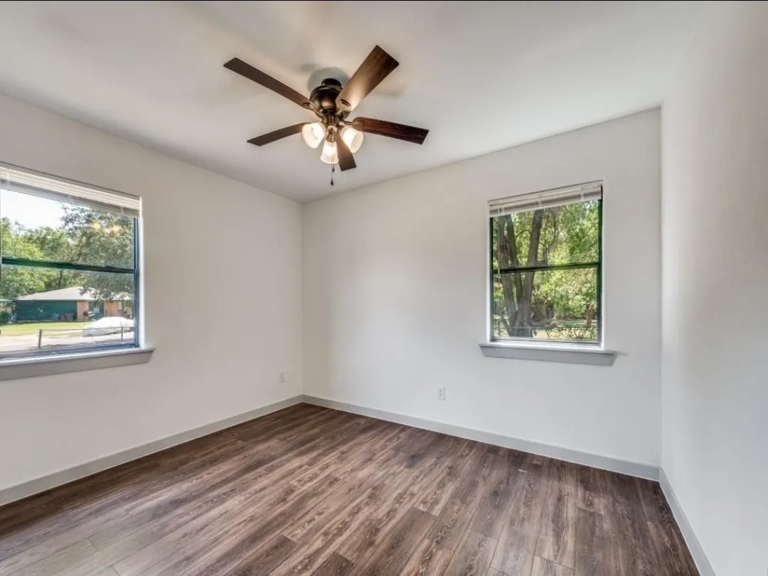 Wood-finish flooring, white walls, two windows, and a ceiling fan with light fixture