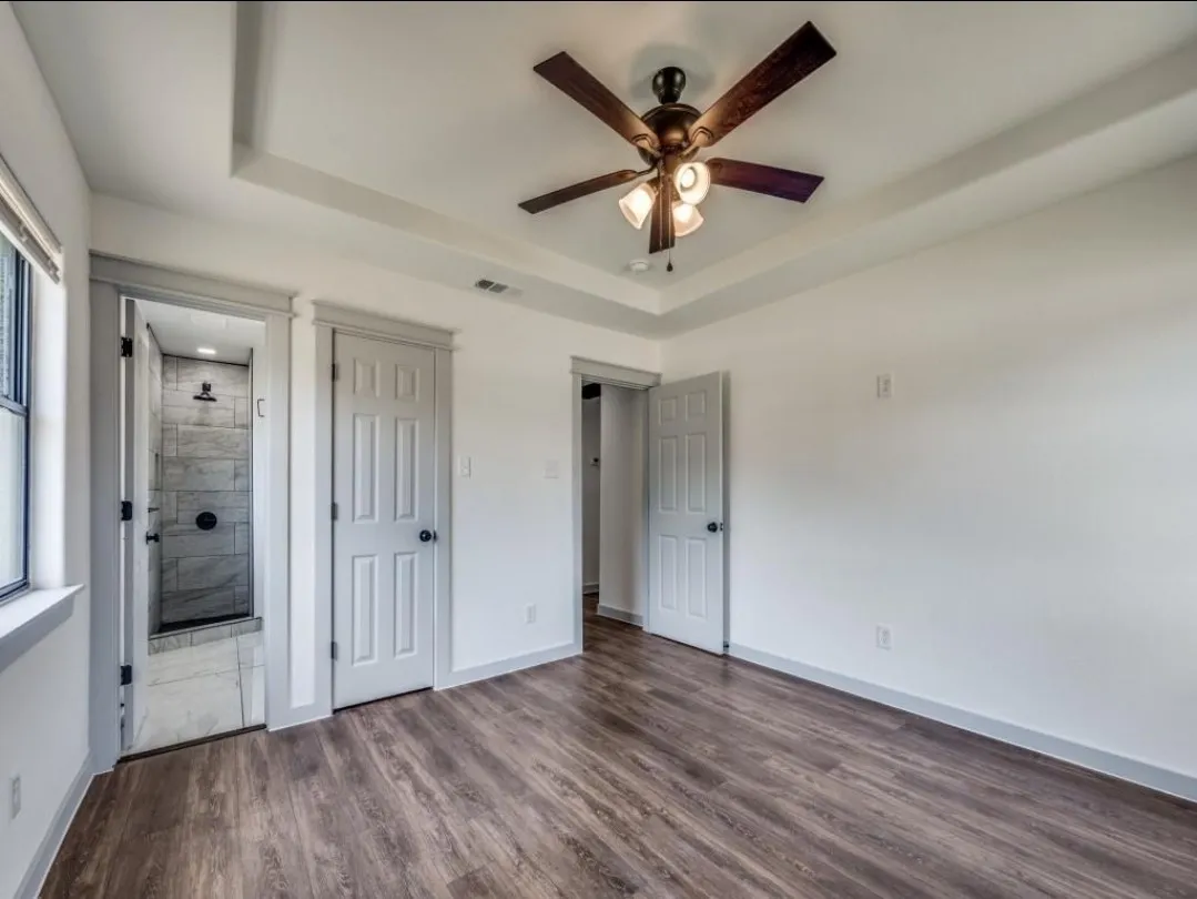 Tray ceiling with ceiling fan, wood-finish flooring, and crisp white walls