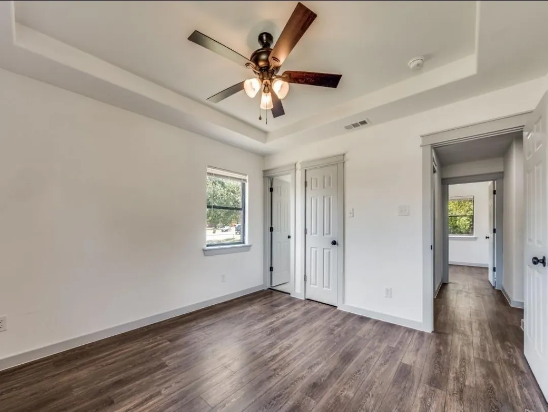 Tray ceiling with a ceiling fan, wood-finish flooring, and white paneled doors