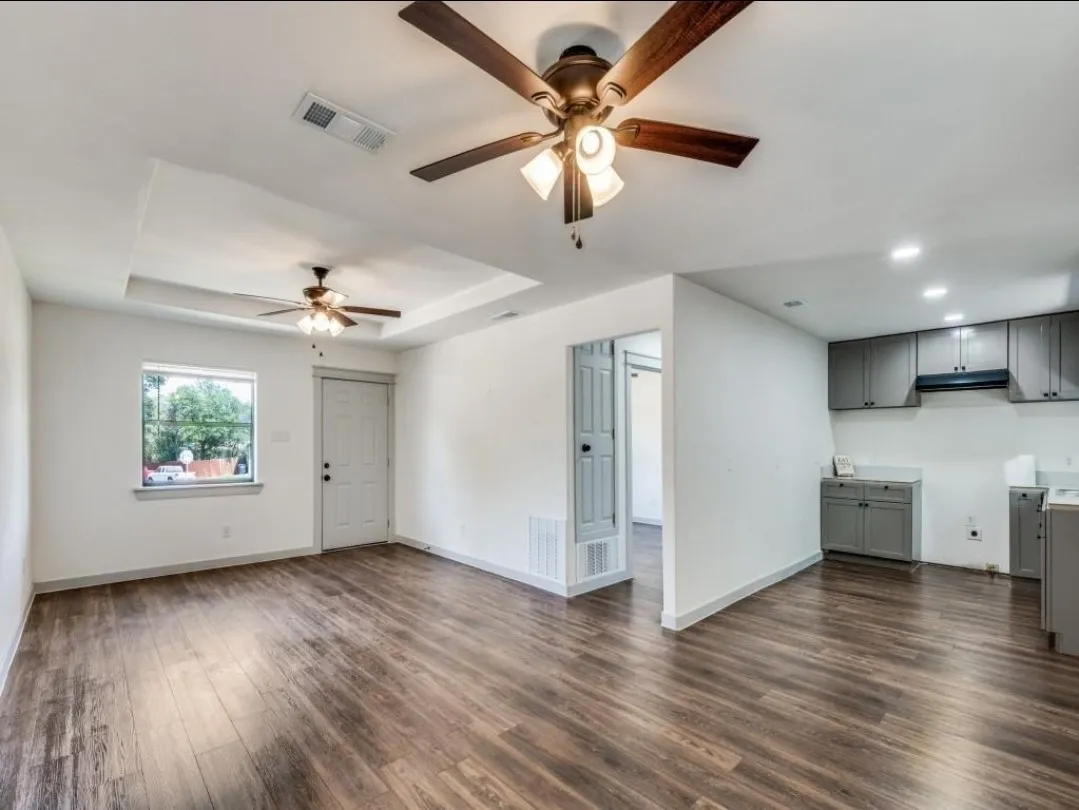 Wood-finish flooring throughout, tray ceiling with a ceiling fan, white paneled door, gray kitchen cabinetry, and recessed lighting