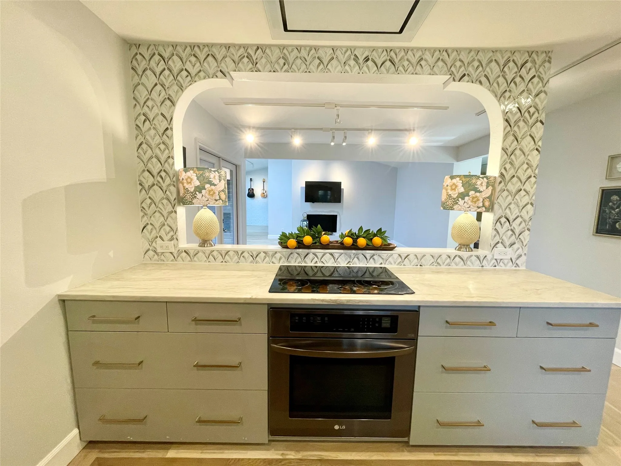Built-in electric cooktop and oven, light-toned countertop, custom cabinetry with linear hardware, patterned tile backsplash, and an arched passthrough