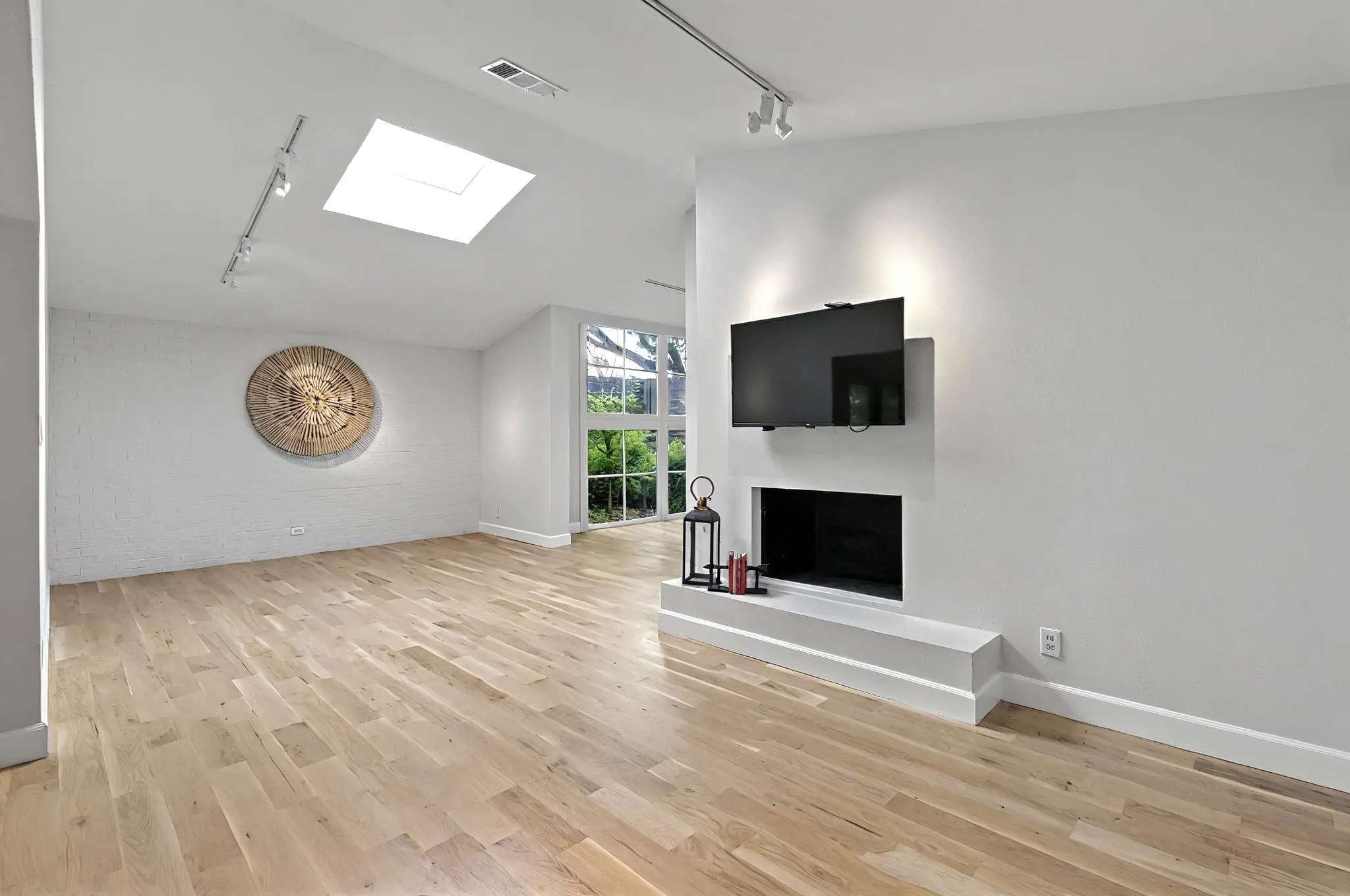 Sloped ceiling with skylight, wood-finish flooring, built-in fireplace, track lighting, and a large window