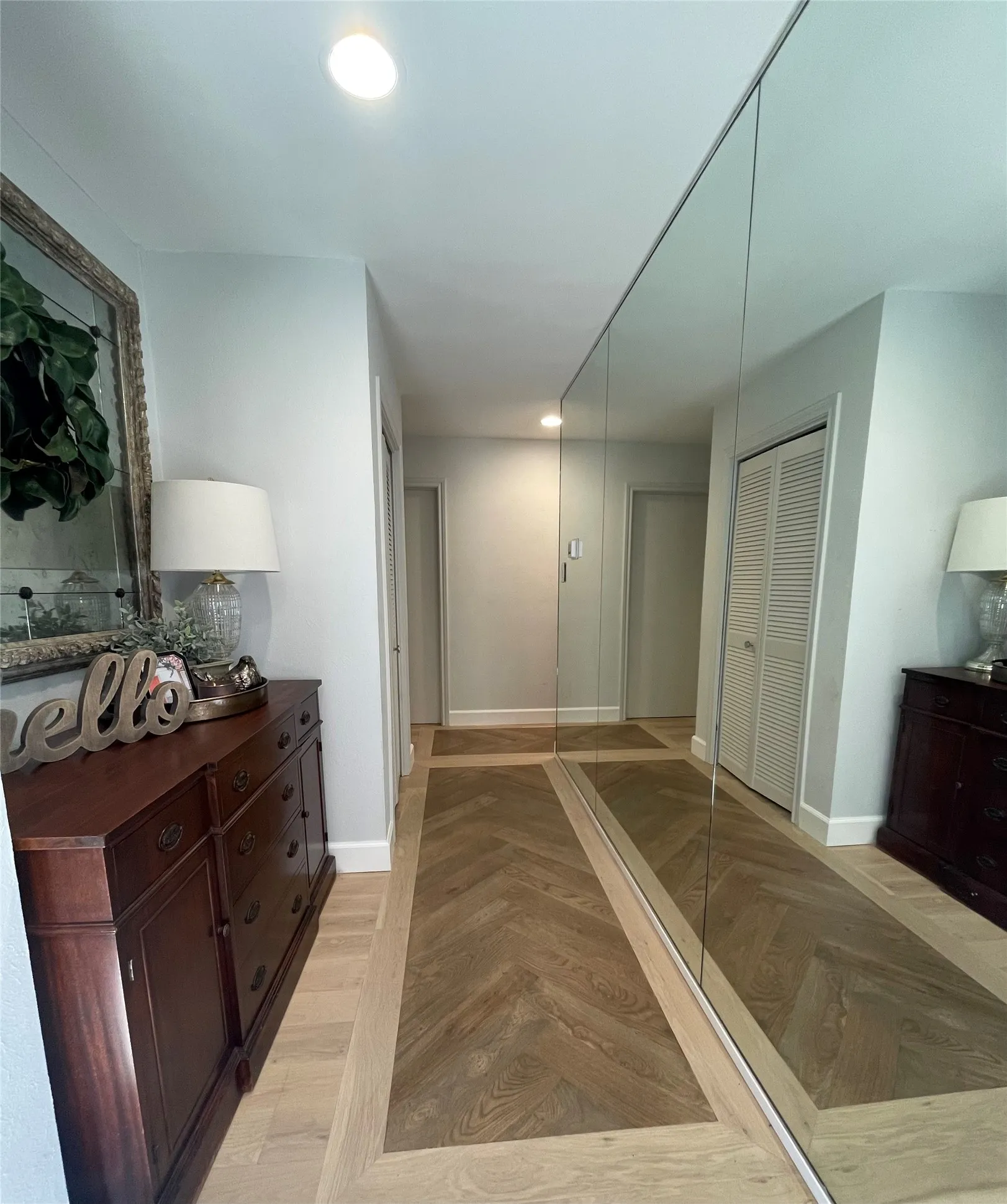 Recessed lighting, light-toned walls, full-height mirrored wall, herringbone wood-finish flooring, and bi-fold closet doors