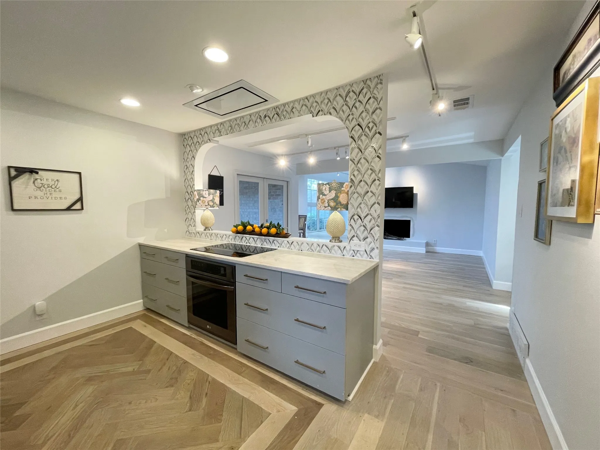 Kitchen island featuring light-toned cabinetry, an integrated cooktop, a built-in oven, and a light-colored countertop