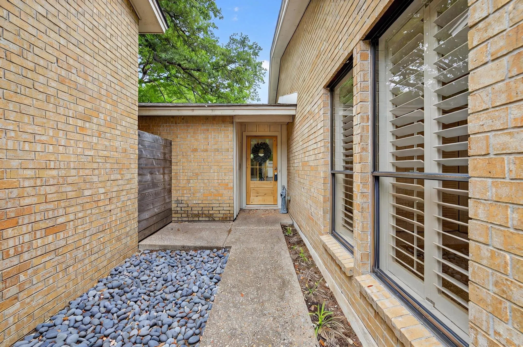 Brick exterior, mature landscaping, concrete walkway, and a wooden entry door