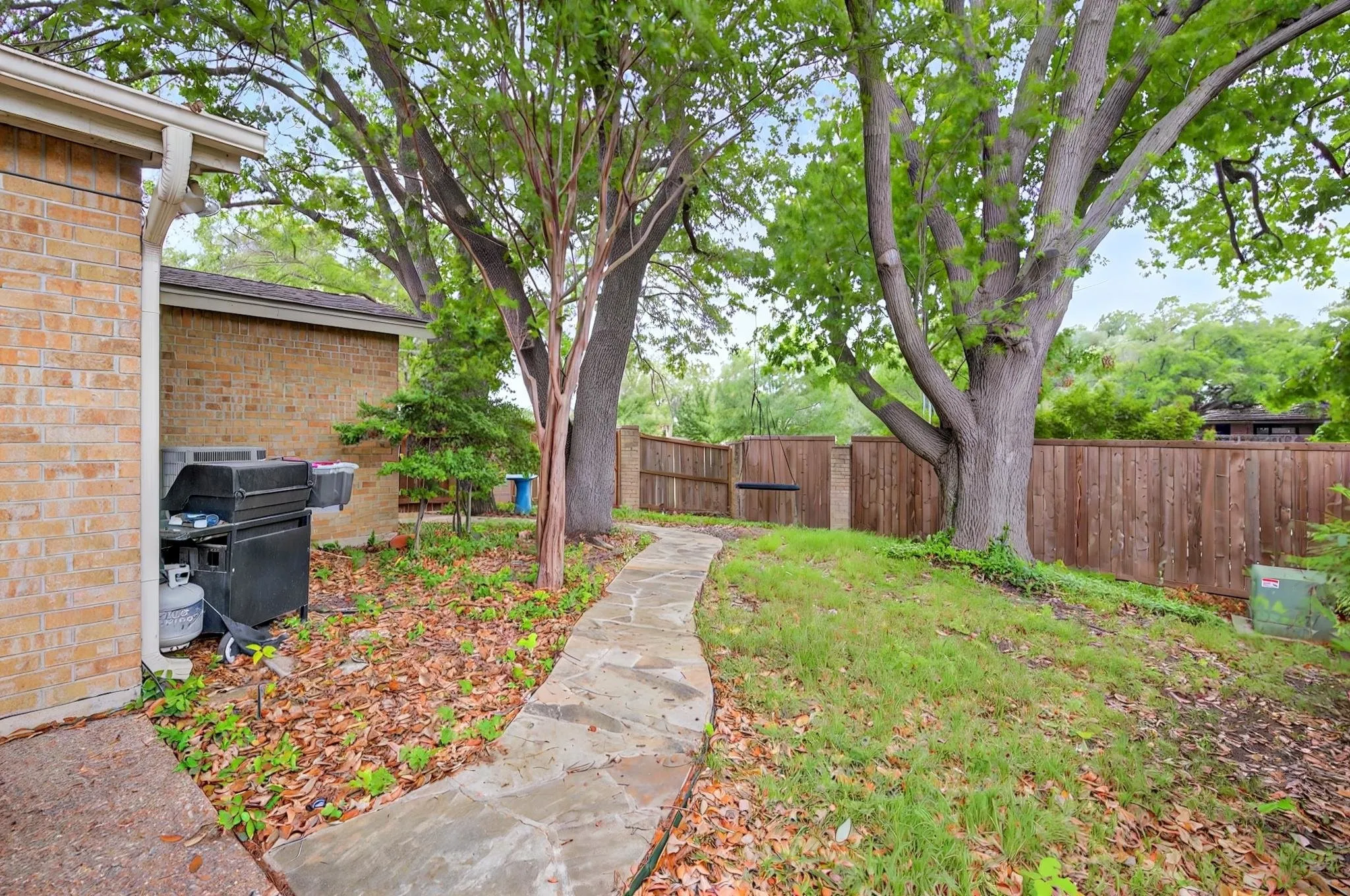 Brick exterior, flagstone pathway, mature trees, wood privacy fence, and sloped grassy area