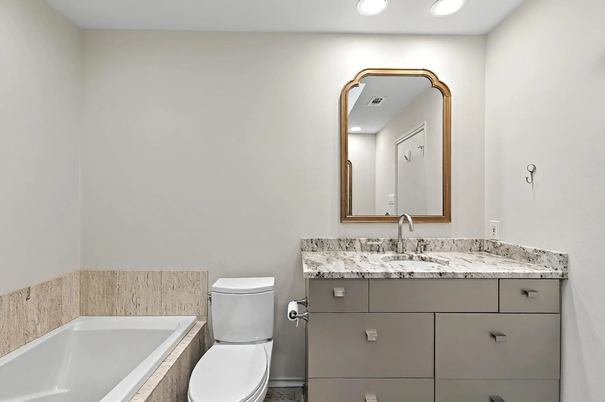 Recessed lighting, vanity with stone countertop, integrated sink, and an ornamental mirror