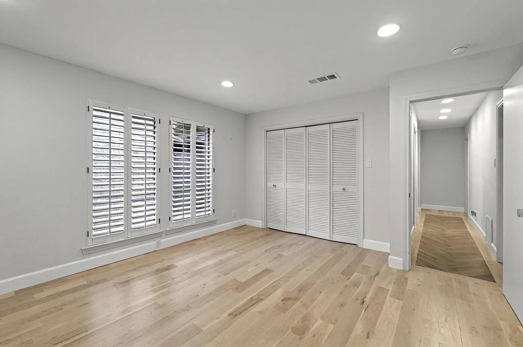 Light wood-finish flooring with white baseboards, twin windows with plantation shutters, louvered bi-fold closet doors, and recessed lighting
