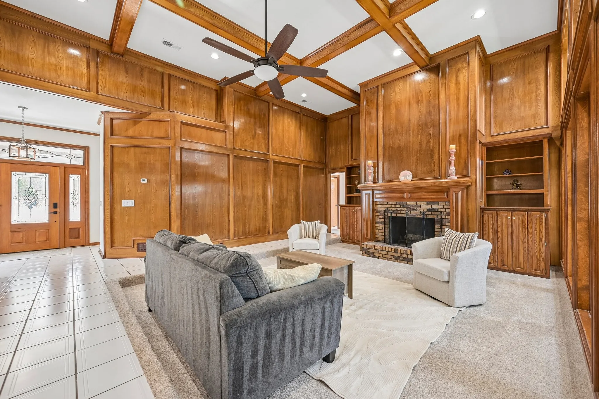Sophisticated great room showcasing exposed wood beam ceiling details, rich wood-finish cabinetry and built-in shelving, a fireplace with surround, and ceramic tile flooring throughout