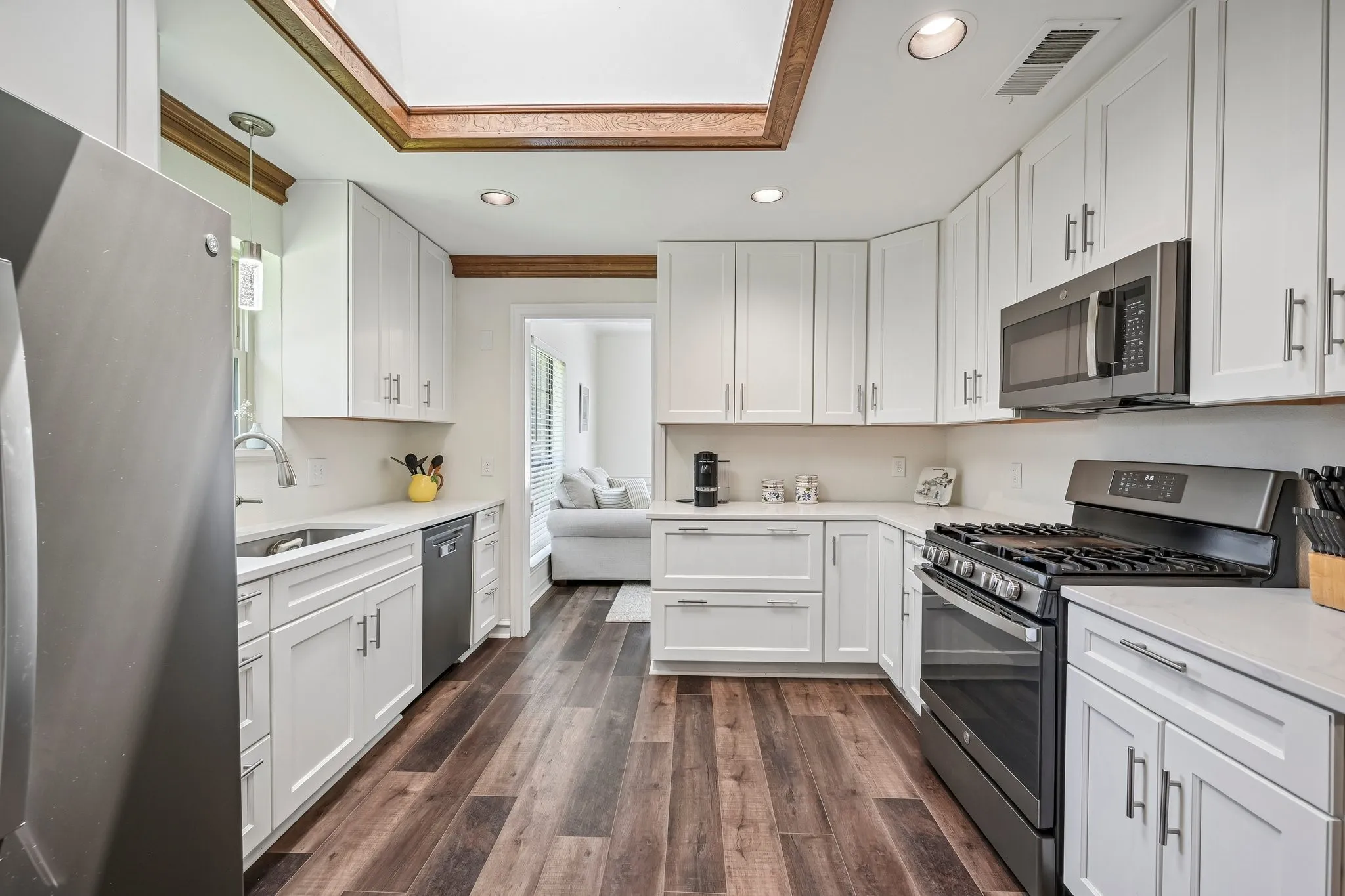Kitchen featuring wood-finish flooring, white cabinetry, integrated stainless steel appliances, light countertops, and a recessed ceiling with wood trim