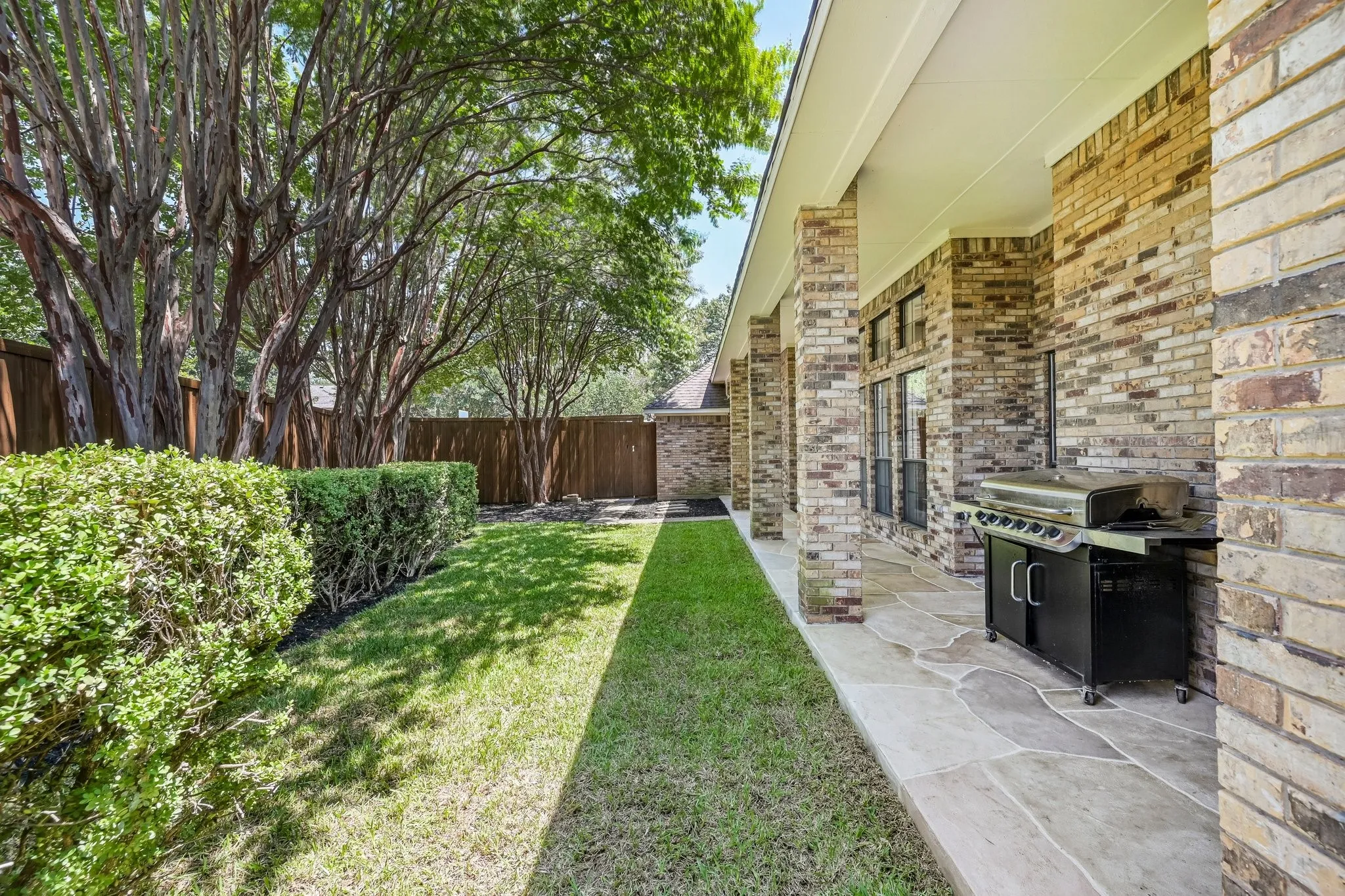 Spacious backyard oasis featuring a manicured lawn, mature shade trees, and professional-grade built-in grill on an extended patio