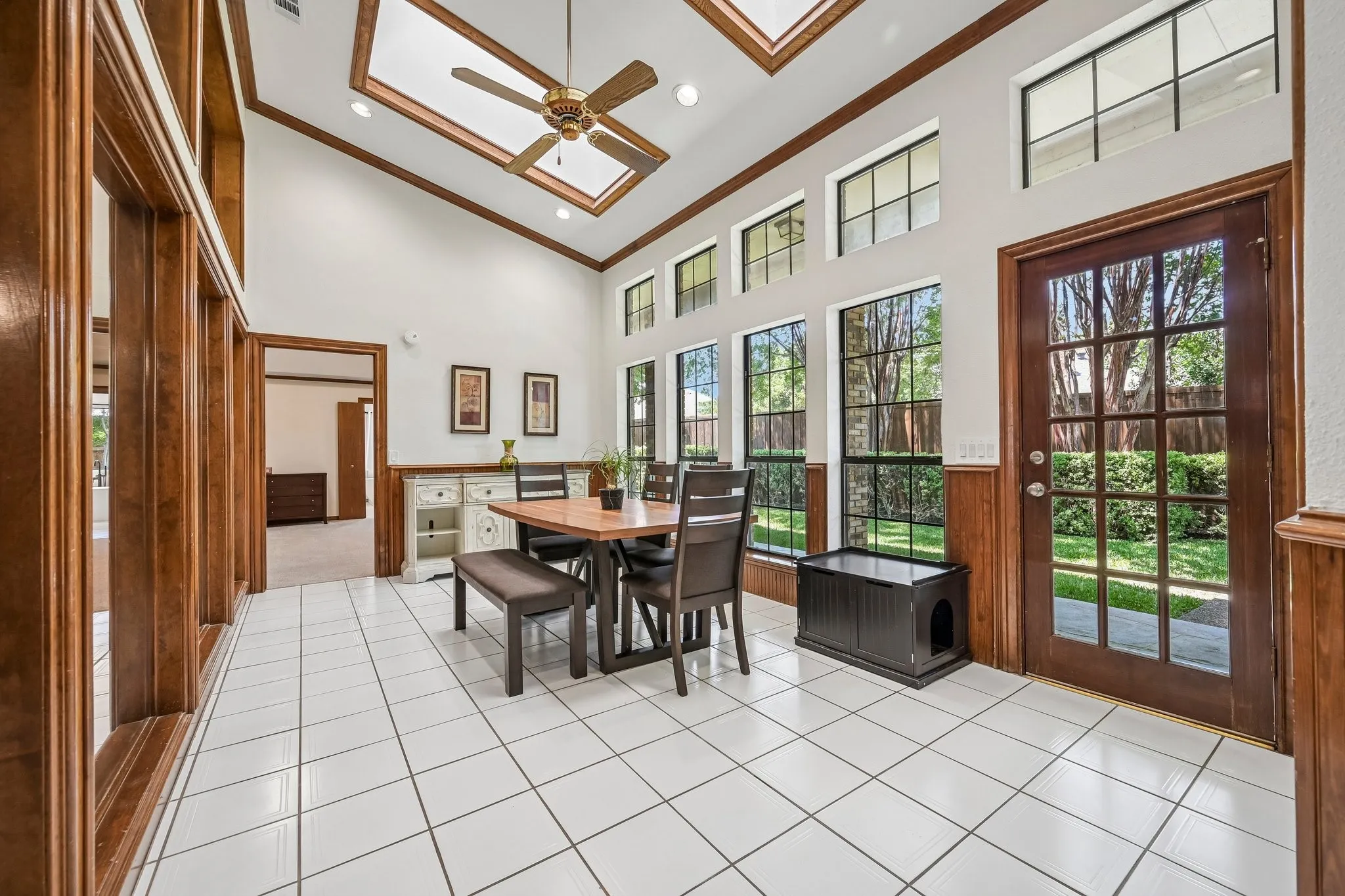 Sunlit sunroom featuring soaring coffered ceilings with skylights, ceramic tile flooring, and French doors opening to outdoor landscape