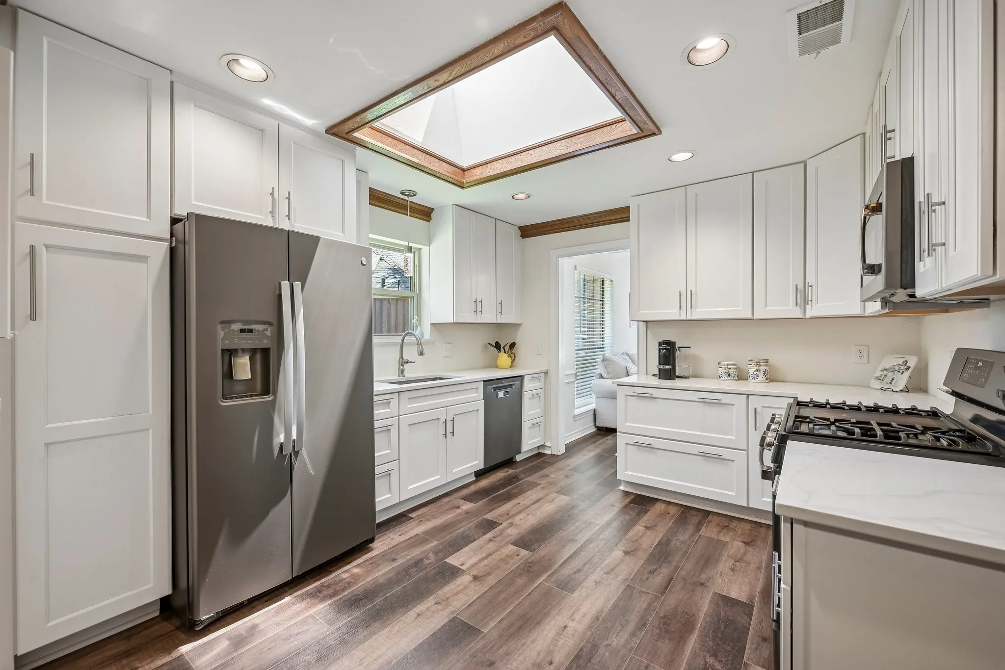 Kitchen featuring wood-finish flooring, white cabinetry, a skylight, and stainless steel appliances