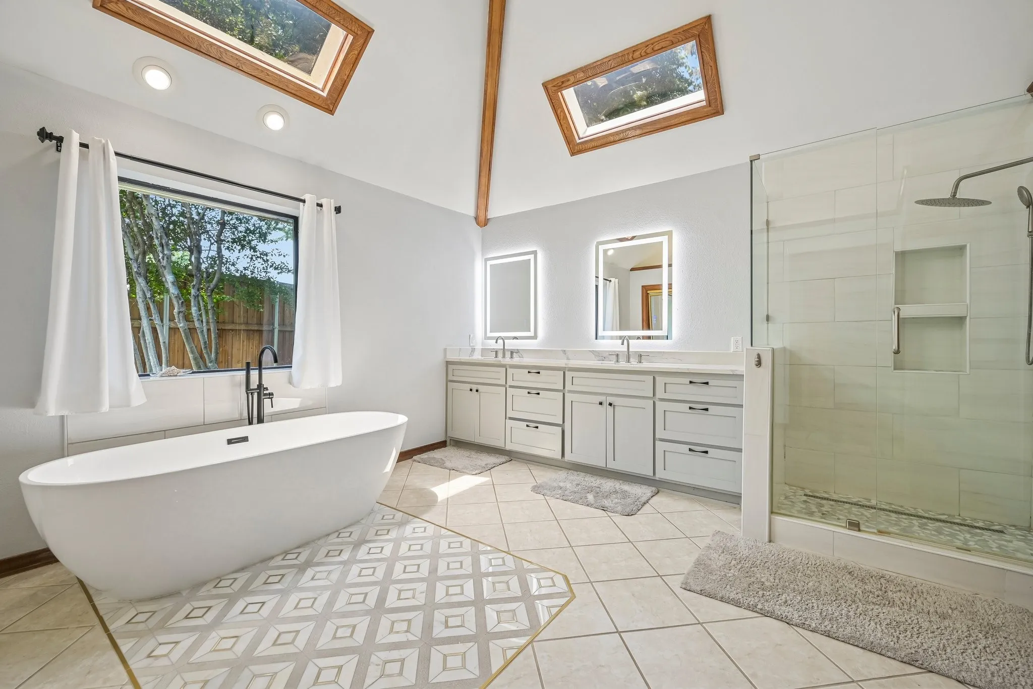 Spa-inspired primary bathroom featuring a freestanding soaking tub, dual-sink vanity with ample storage and integrated lighting mirrors, and a frameless glass-enclosed shower with tile surround
