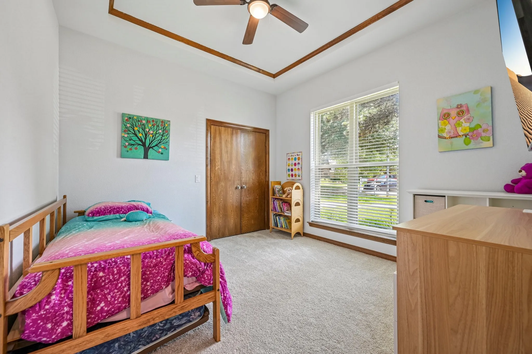 Bright bedroom featuring wood-frame twin bed, carpeted flooring, vaulted ceiling with ceiling fan, large sliding glass doors with natural light, and wood-finish dresser with storage