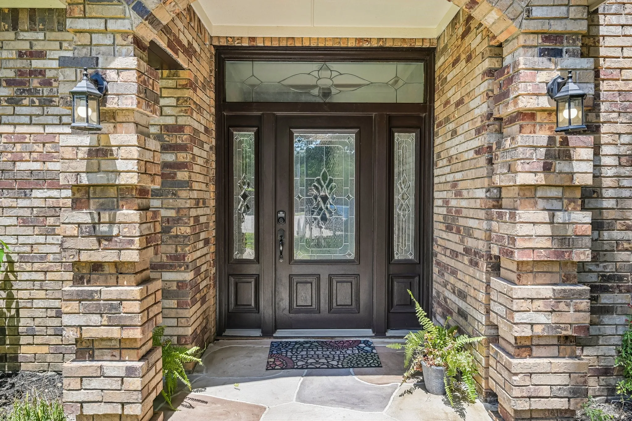 Welcoming entry features a dark-finish steel door with decorative glass panels and sidelights, framed by multi-toned brick masonry in warm earth tones